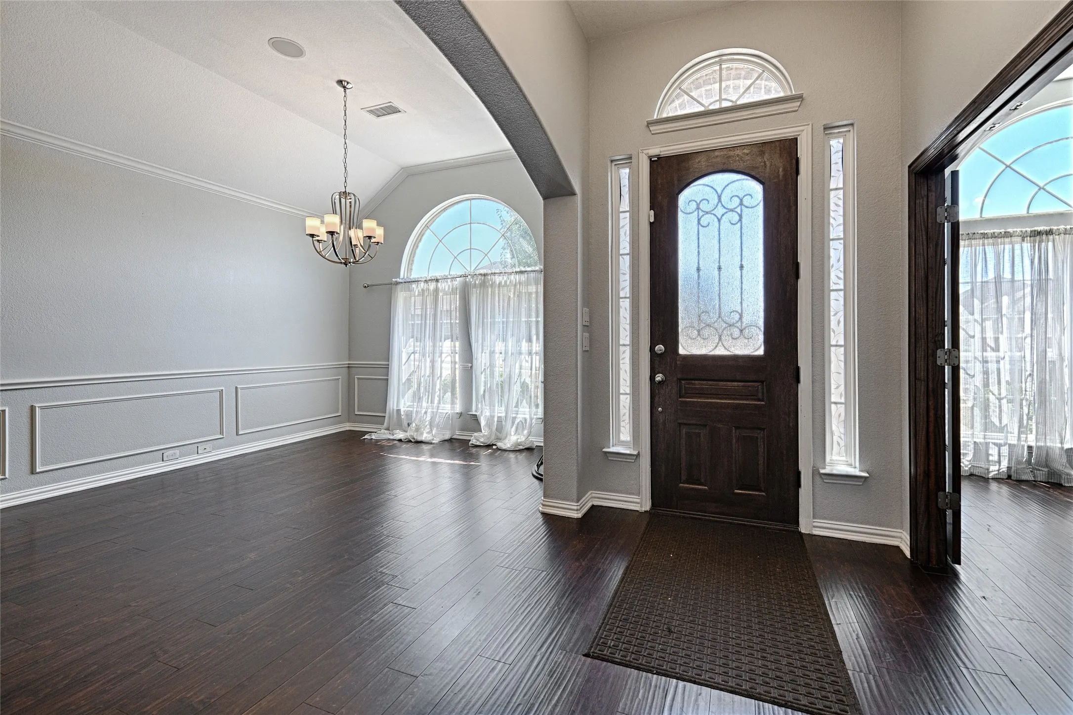 Dark wood-finish flooring throughout, decorative wainscoting, arched windows with transoms, and a vaulted ceiling with a chandelier