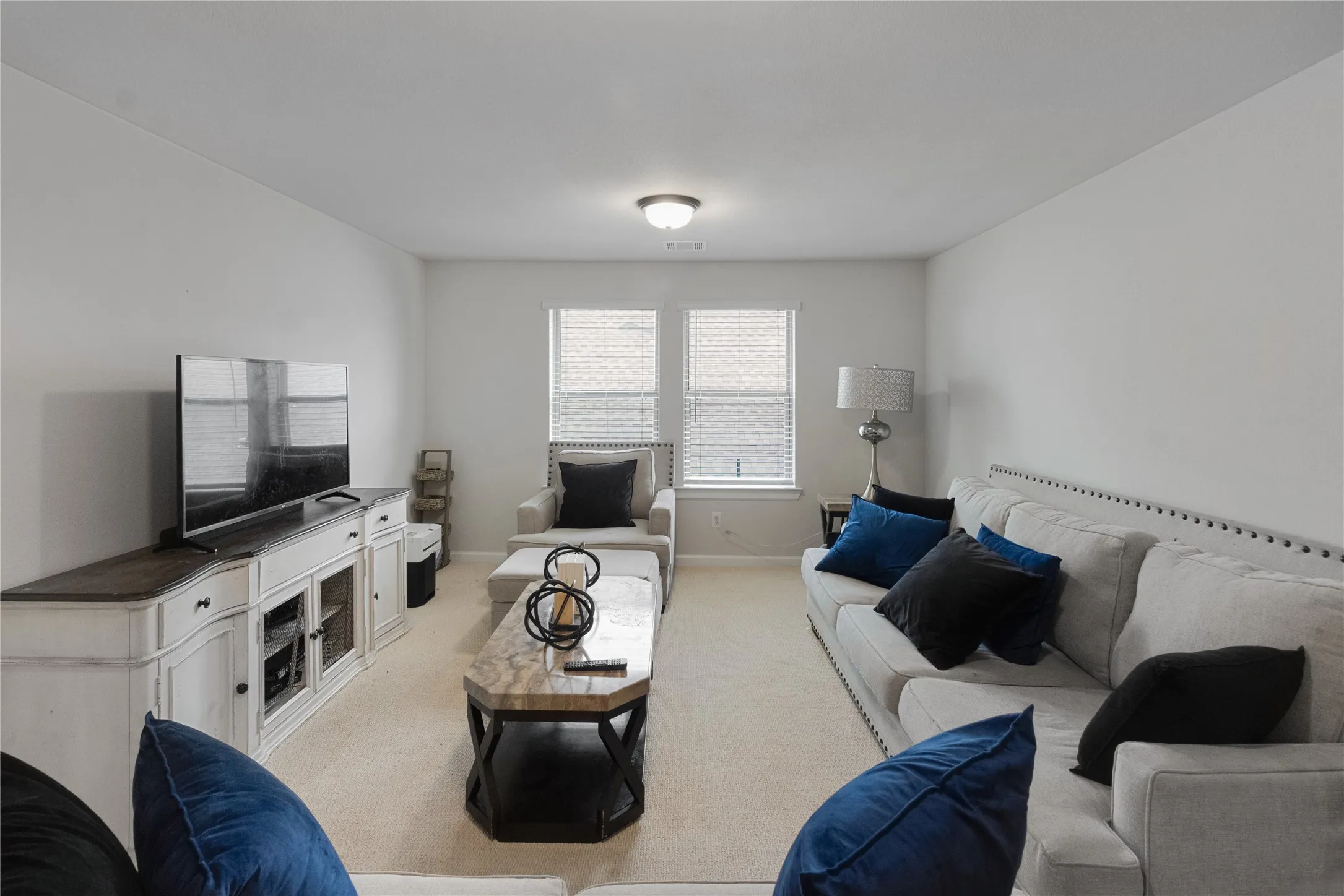 Carpeted interior space featuring two windows with blinds and a ceiling-mounted light fixture