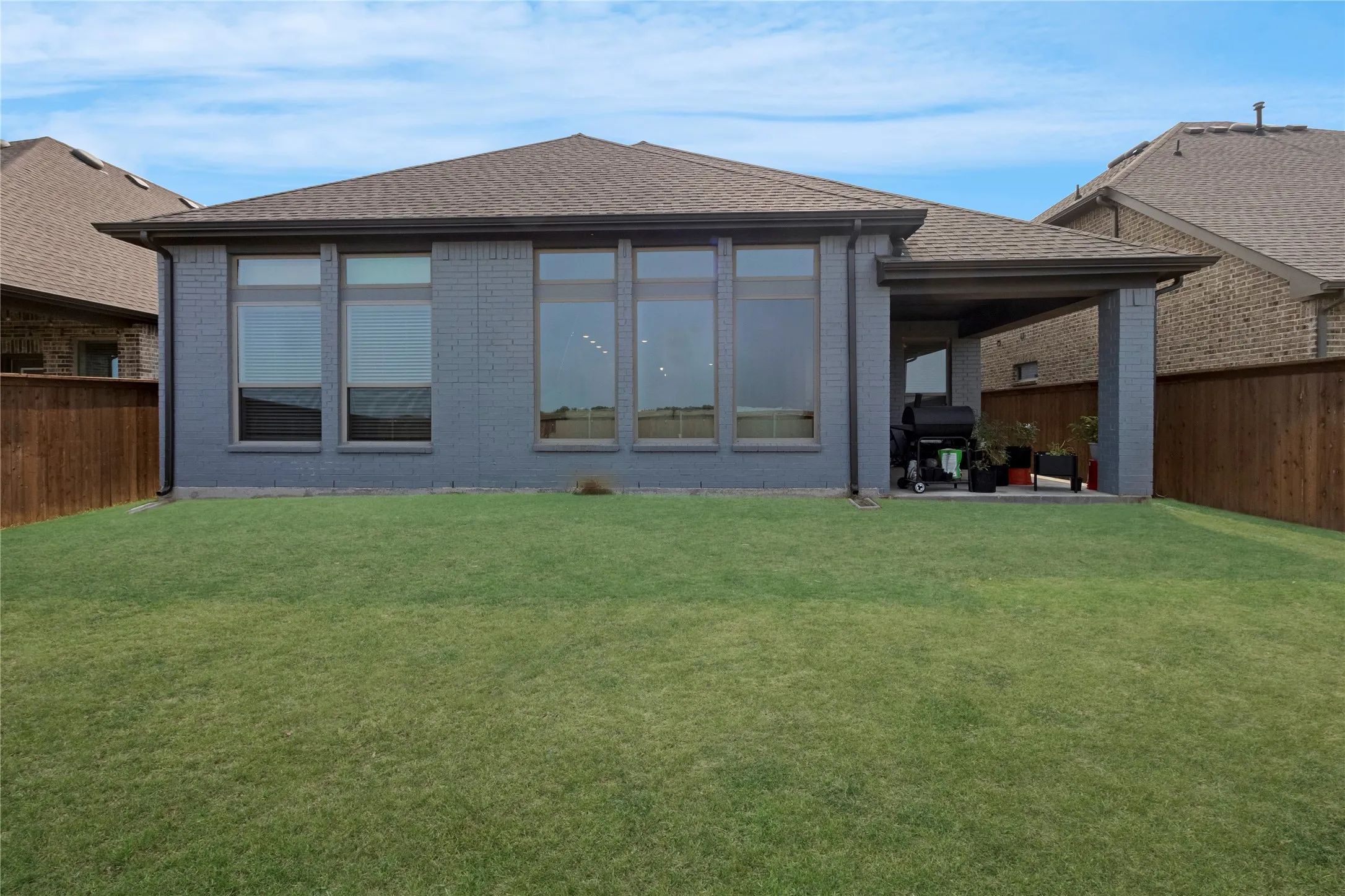 Expansive backyard with a manicured lawn, full-height privacy fencing, and a covered patio