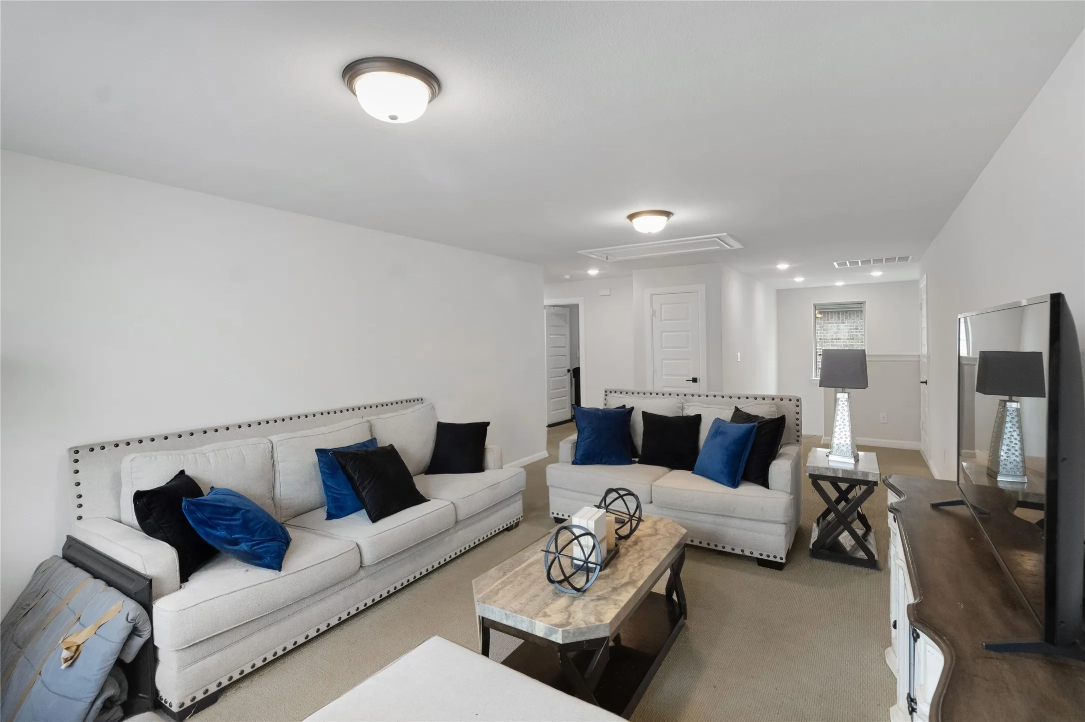 Recessed lighting and ceiling-mounted fixtures illuminate this spacious room with light-toned walls and carpeting