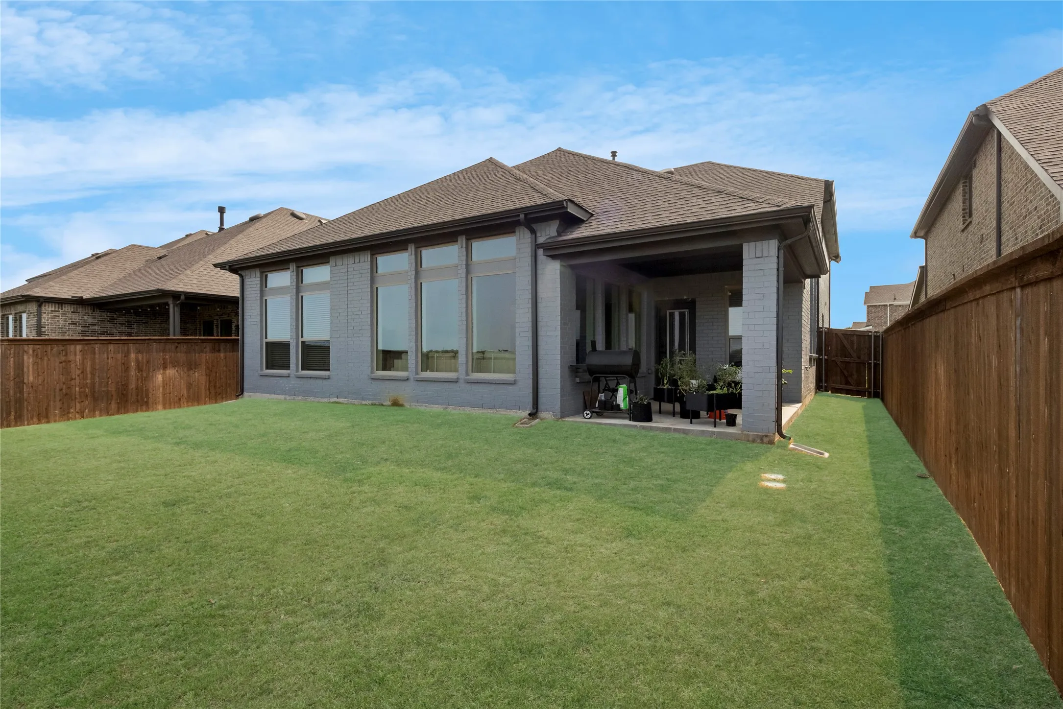 Expansive grassy yard with a covered patio, brick exterior, and tall privacy fencing