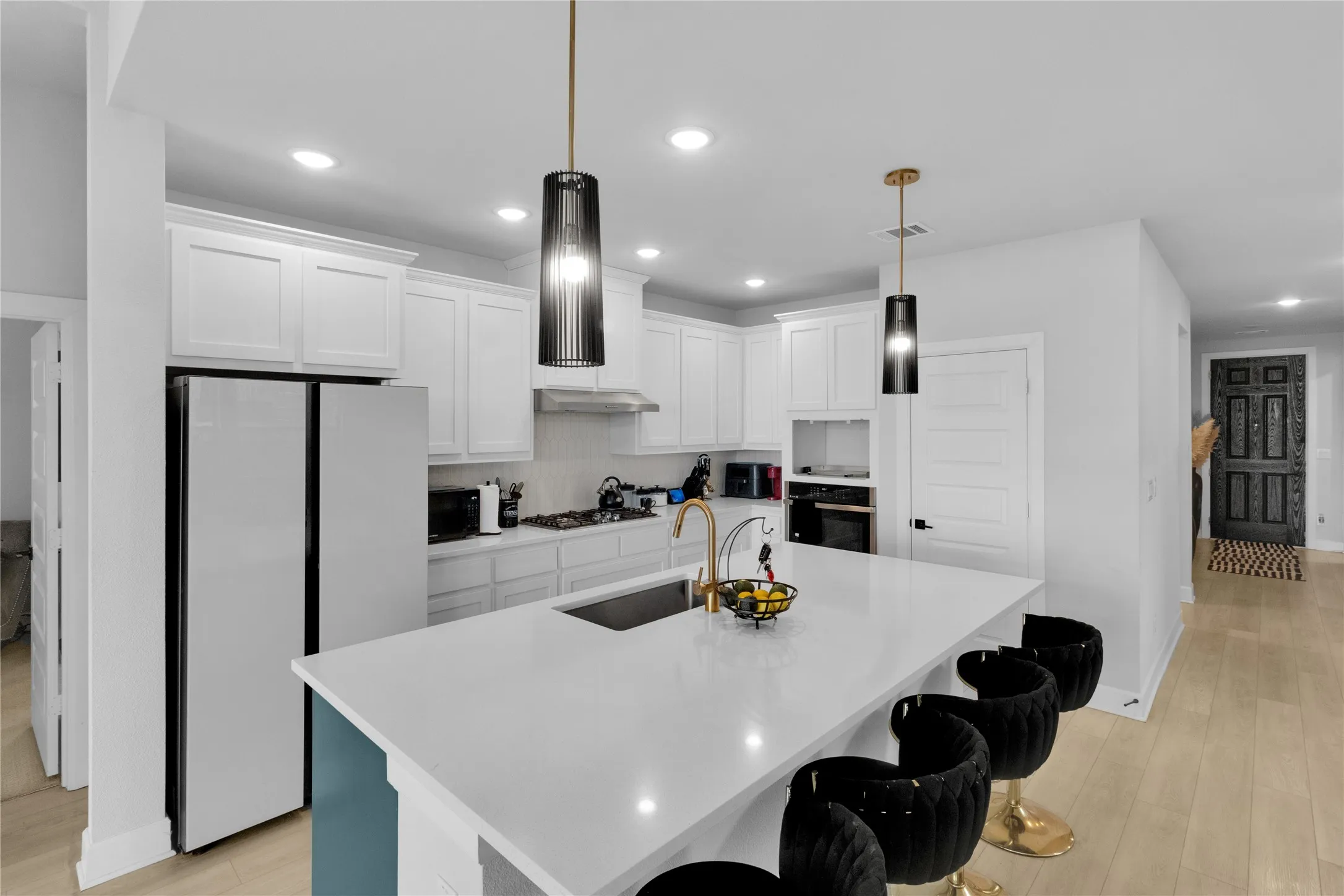 Modern kitchen with white cabinetry, stainless steel appliances, central island with seating, pendant lighting, and light wood-finish flooring