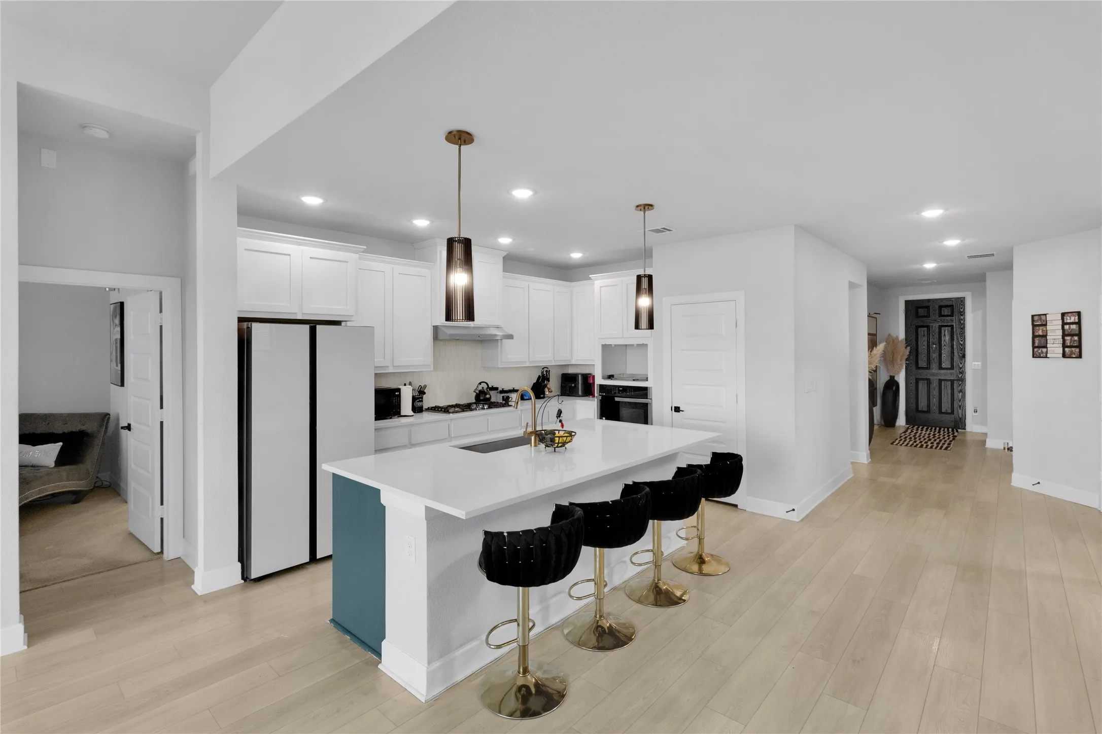 White cabinetry with gold hardware, recessed lighting, wood-finish flooring, kitchen island with seating, and stainless steel appliances