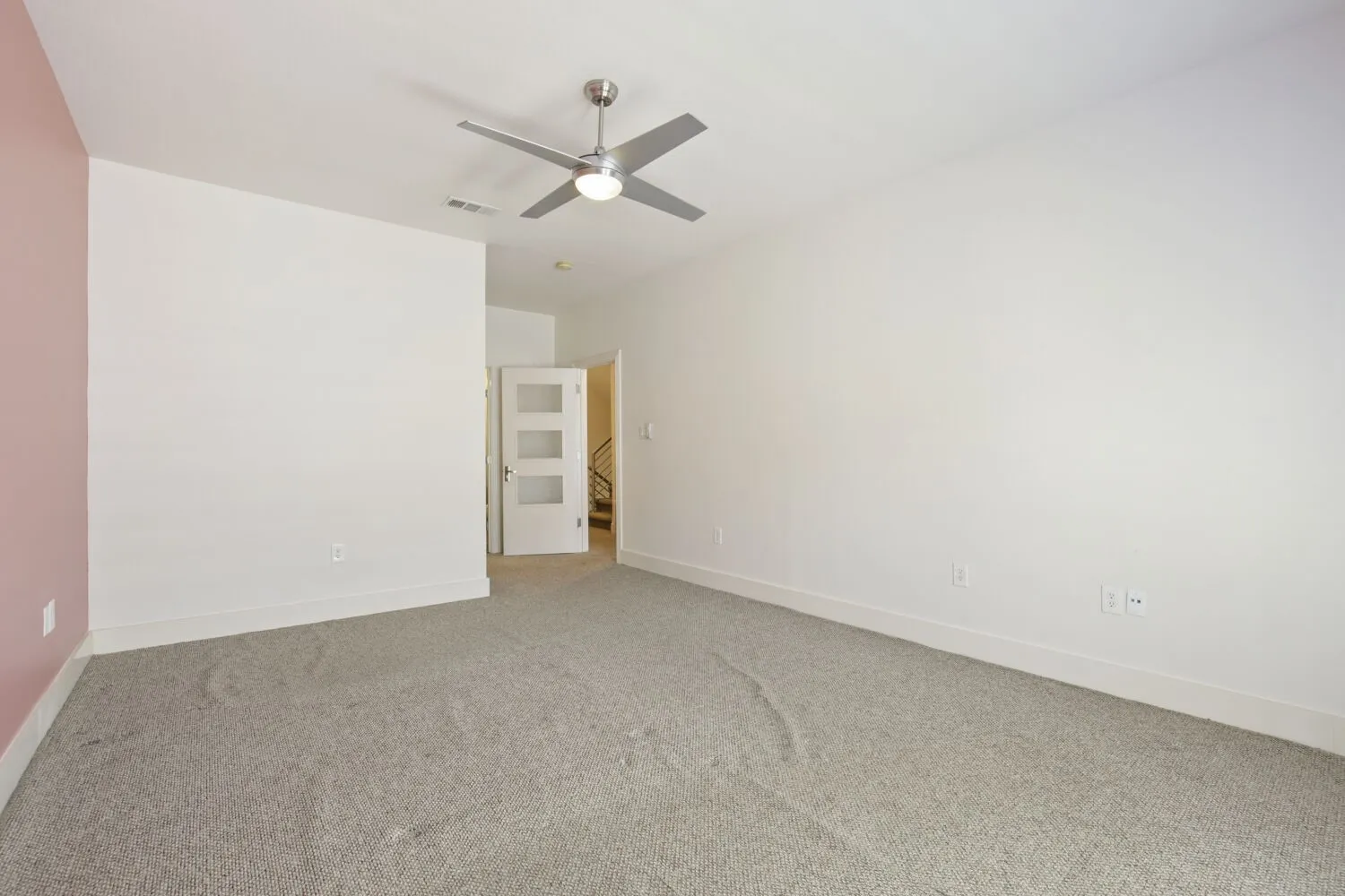 Neutral carpeted flooring with white baseboards, a ceiling fan with integrated lighting, and a white interior door featuring three frosted glass panels