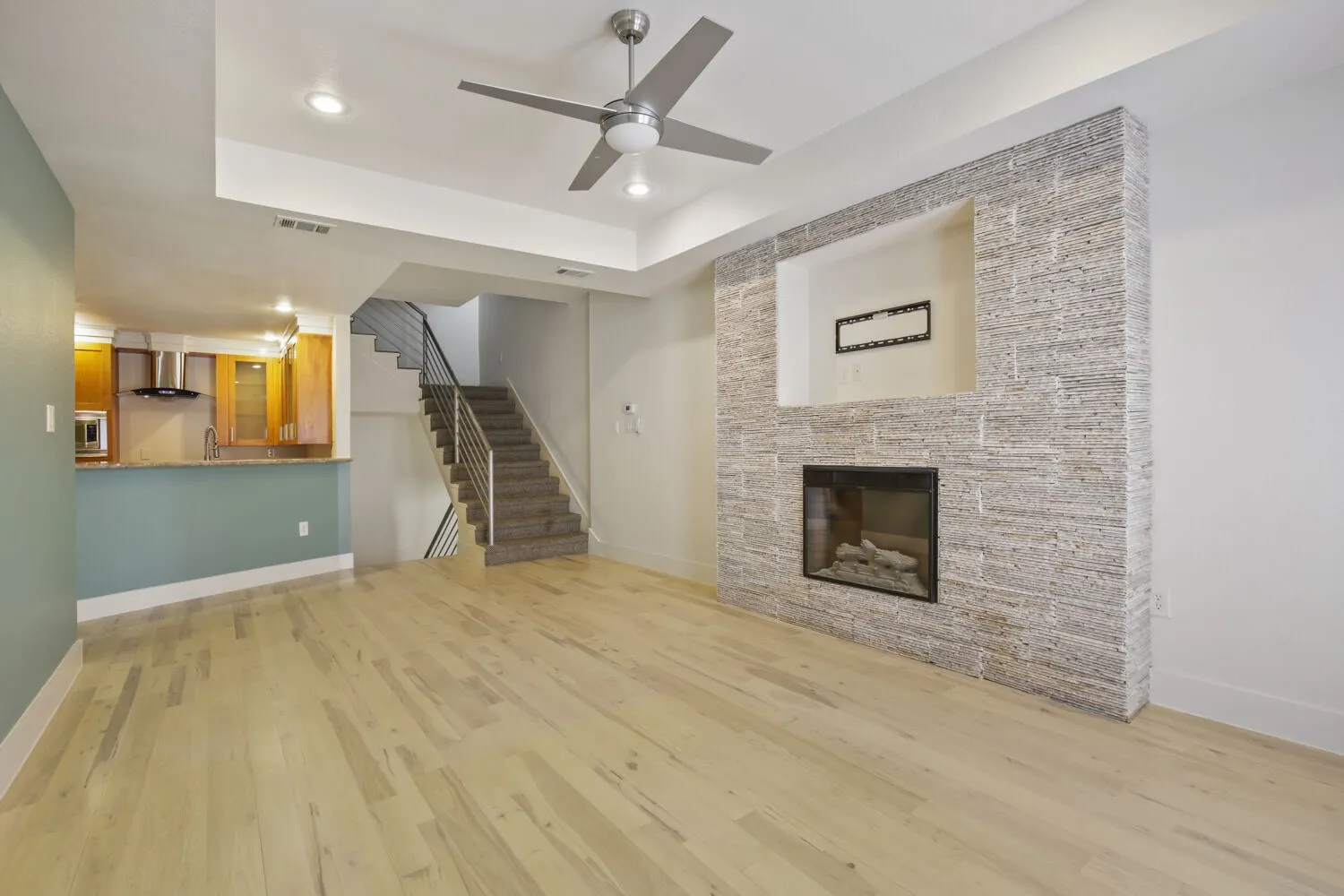 Hardwood-style flooring throughout, modern ceiling fan, recessed lighting, and a contemporary fireplace with a stone surround