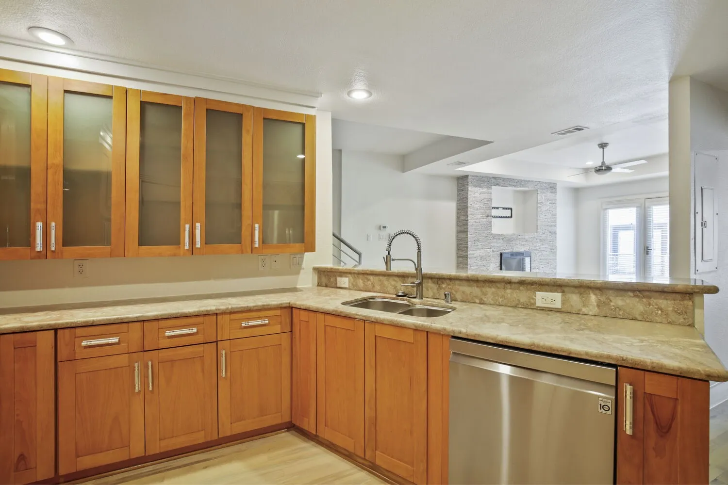 Wood cabinetry with frosted glass upper doors, stainless steel double basin sink, stainless steel dishwasher, and stone countertops