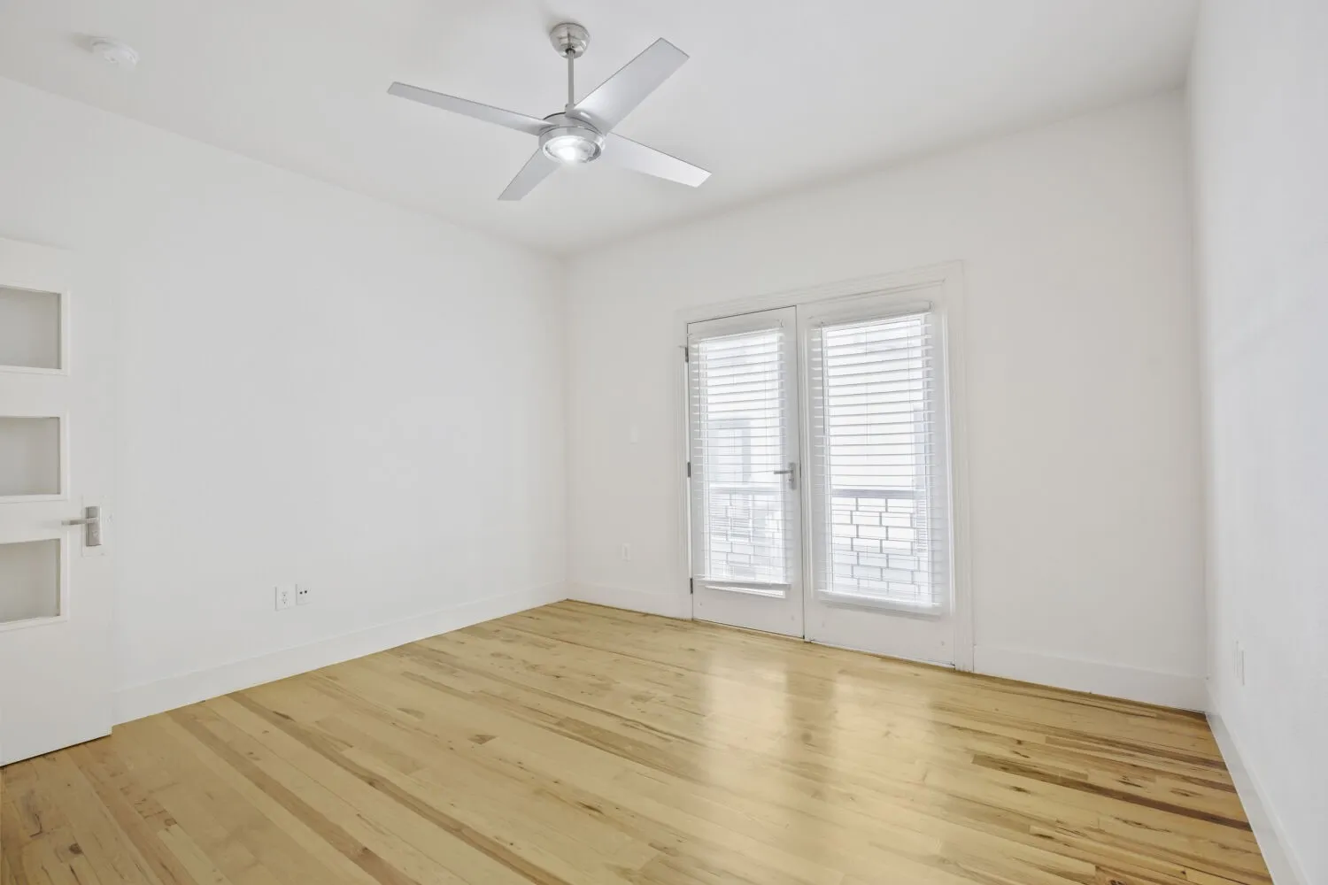 Hardwood flooring, white walls, modern ceiling fan with integrated lighting, glass panel door, and French doors with blinds