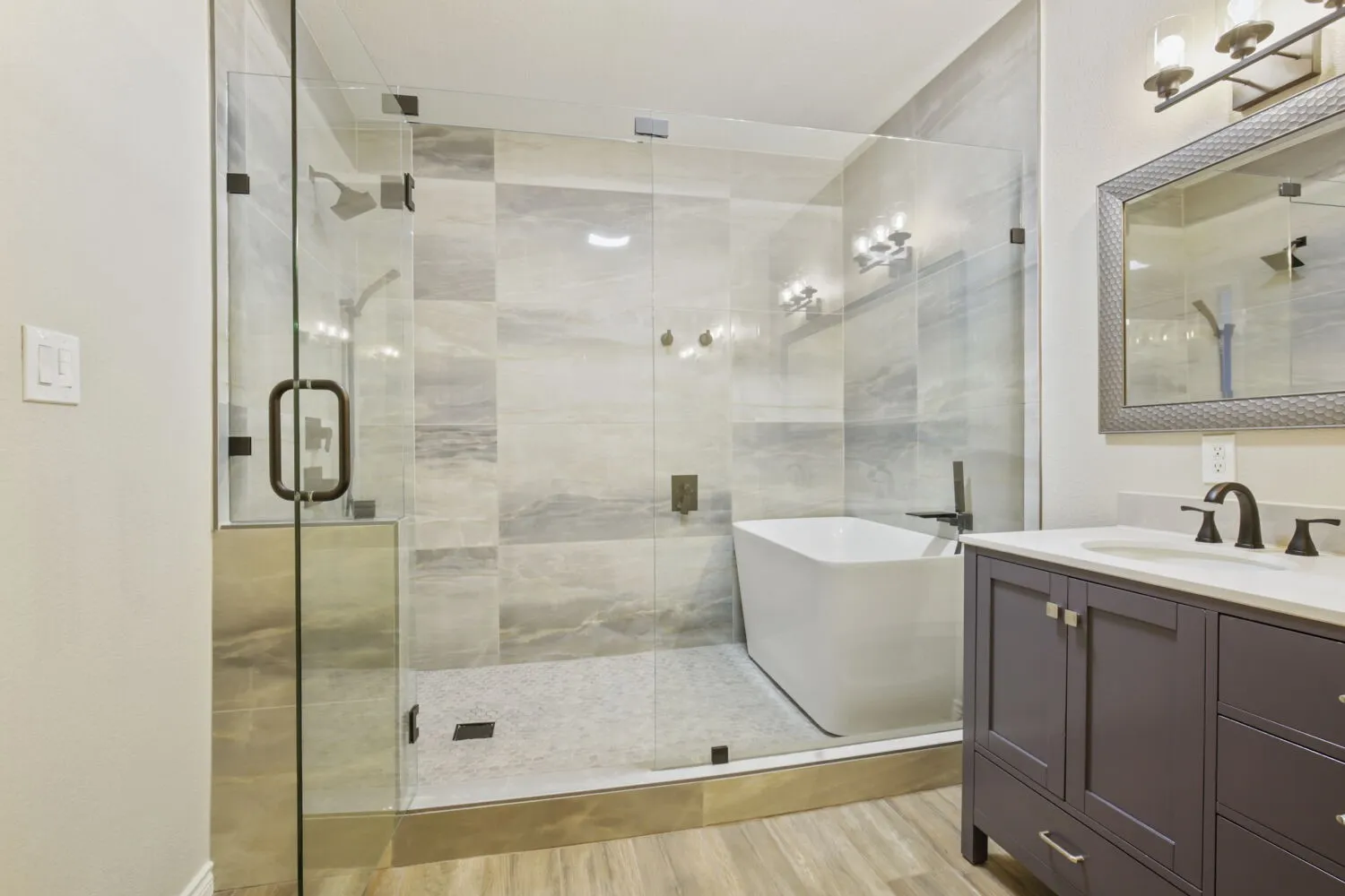 Glass-enclosed shower with a freestanding soaking tub, large format tile walls, and a separate vanity featuring a rectangular sink with dark bronze fixtures