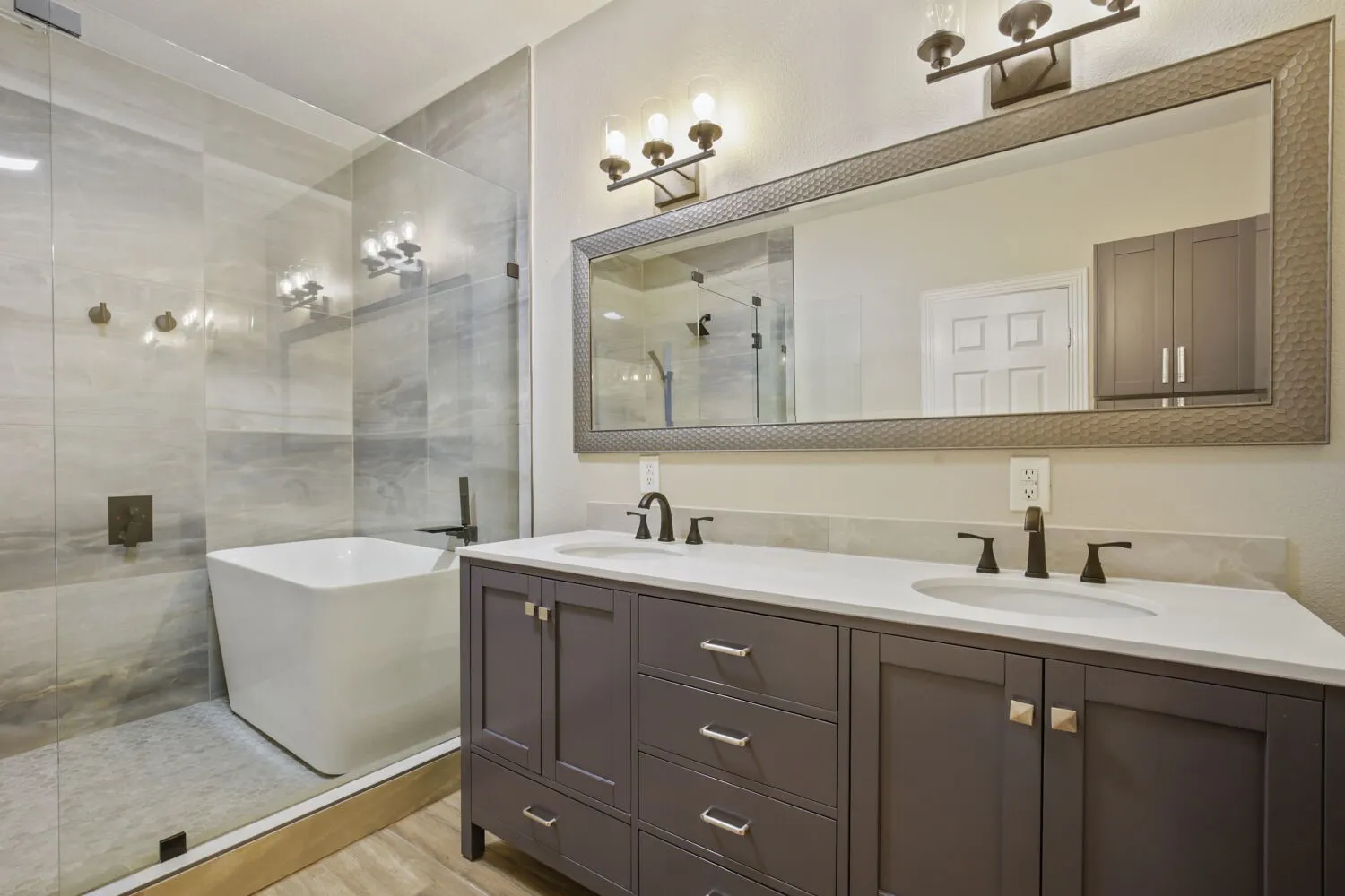 Spacious bathroom featuring a dual vanity with undermount sinks, a freestanding tub, a glass-enclosed shower, and wood-finish flooring