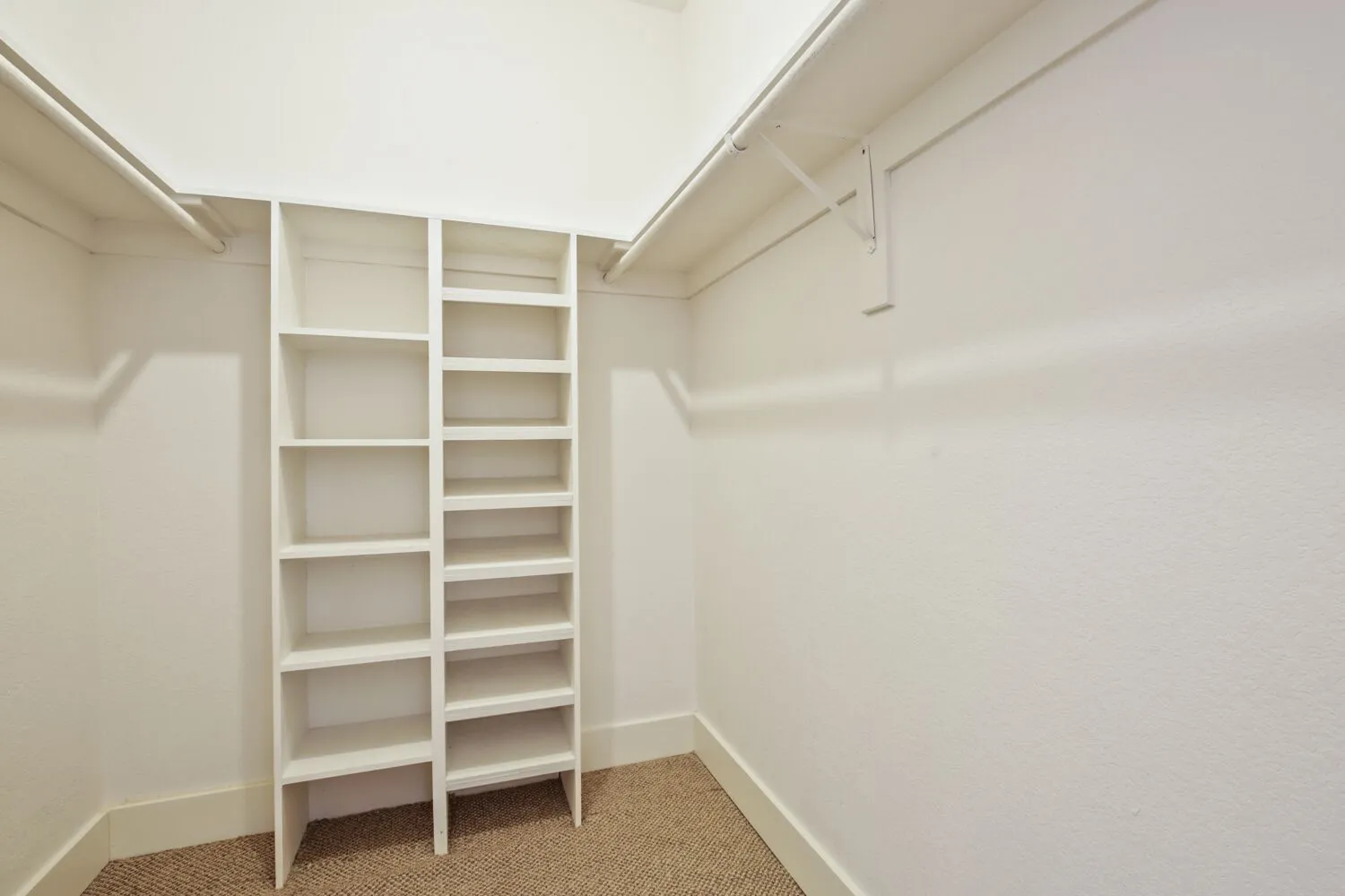Built-in shelving, hanging rods, and carpet flooring within a white-painted interior