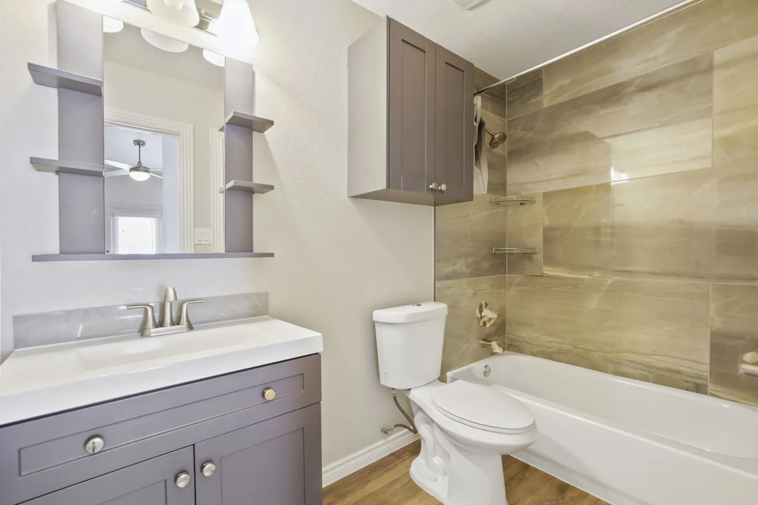 Bathroom with a white bathtub, large format wall tiling, wood-finish flooring, a vanity with under-sink cabinetry, and a mirrored medicine cabinet with integrated shelving