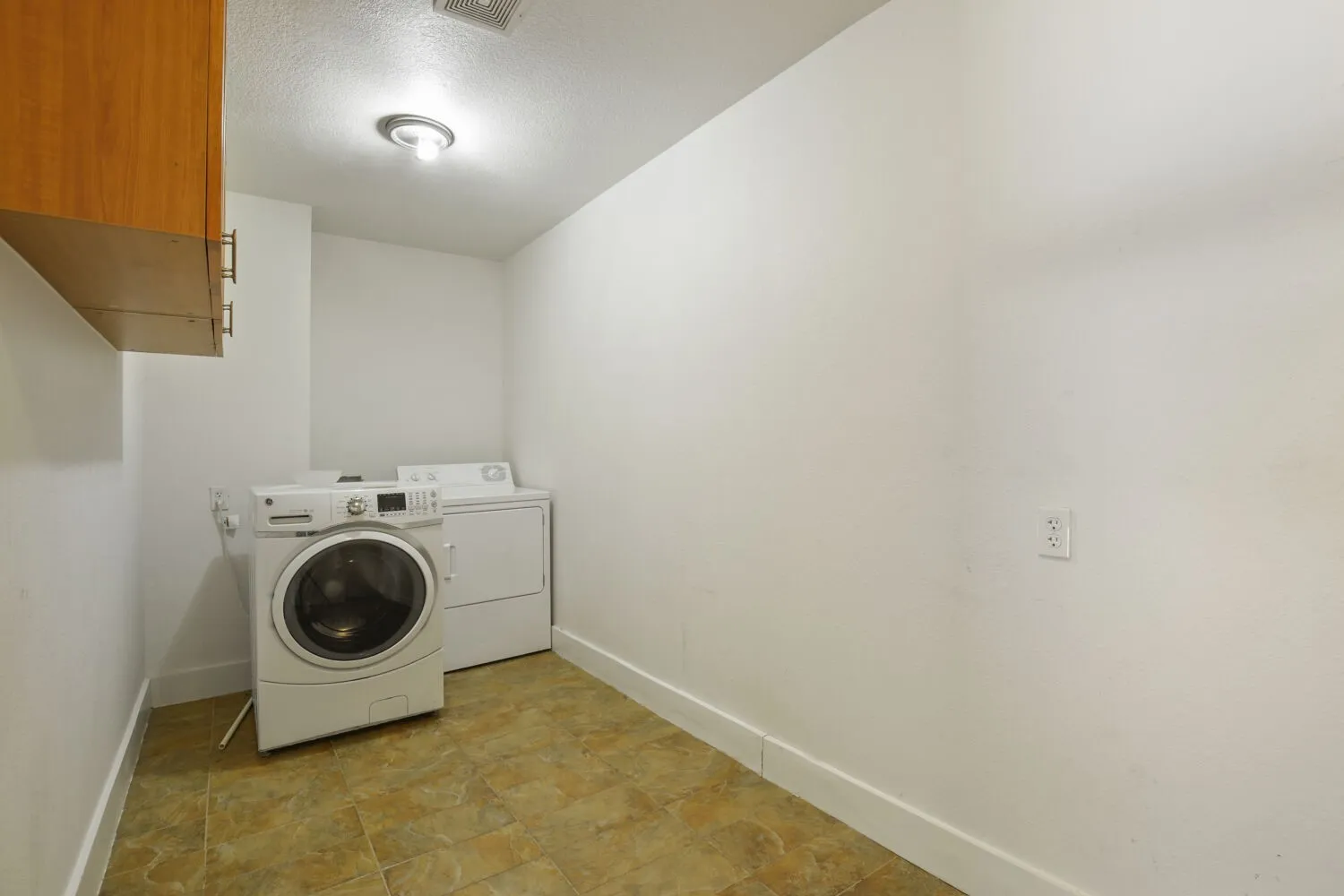 Dedicated laundry space featuring overhead wood-finish cabinetry, tile flooring, and a ceiling-mounted light fixture