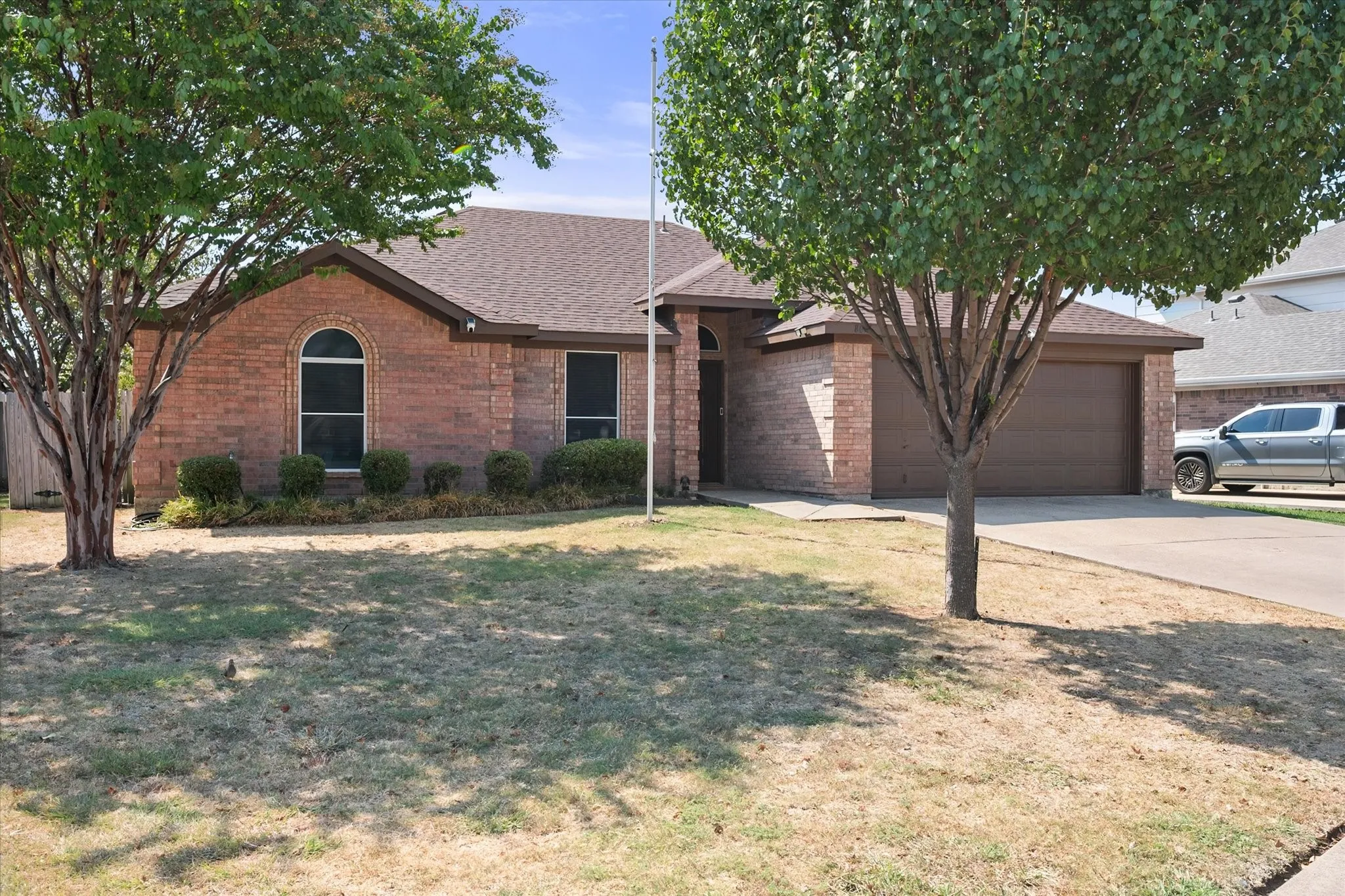 Brick exterior, arched window, attached garage, concrete driveway, mature trees