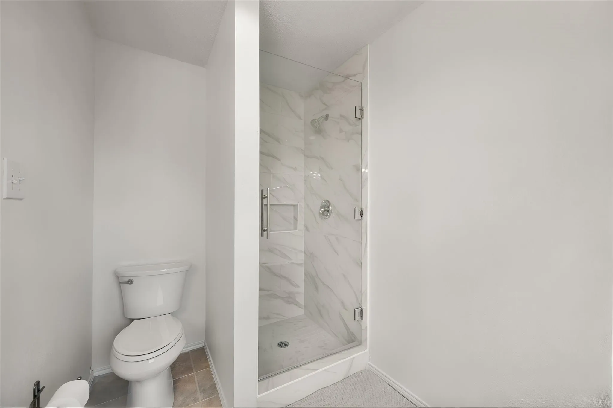 Glass-enclosed shower with a tiled interior, featuring a built-in shelf and chrome fixtures
