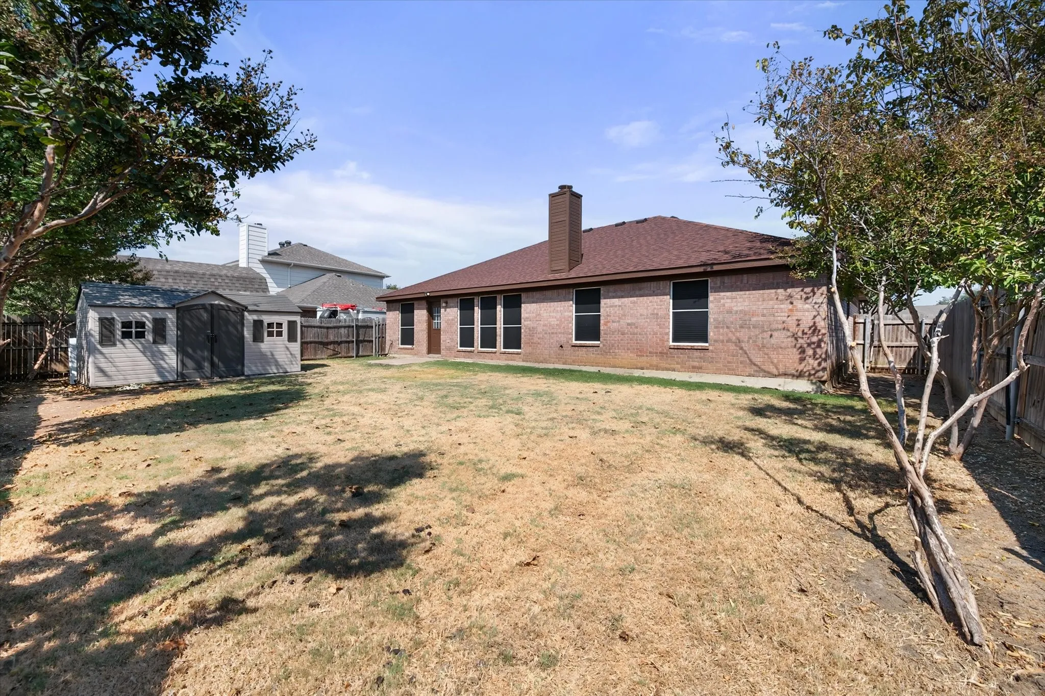 Expansive backyard featuring a brick exterior, brown shingled roof, built-in chimney, and a storage shed
