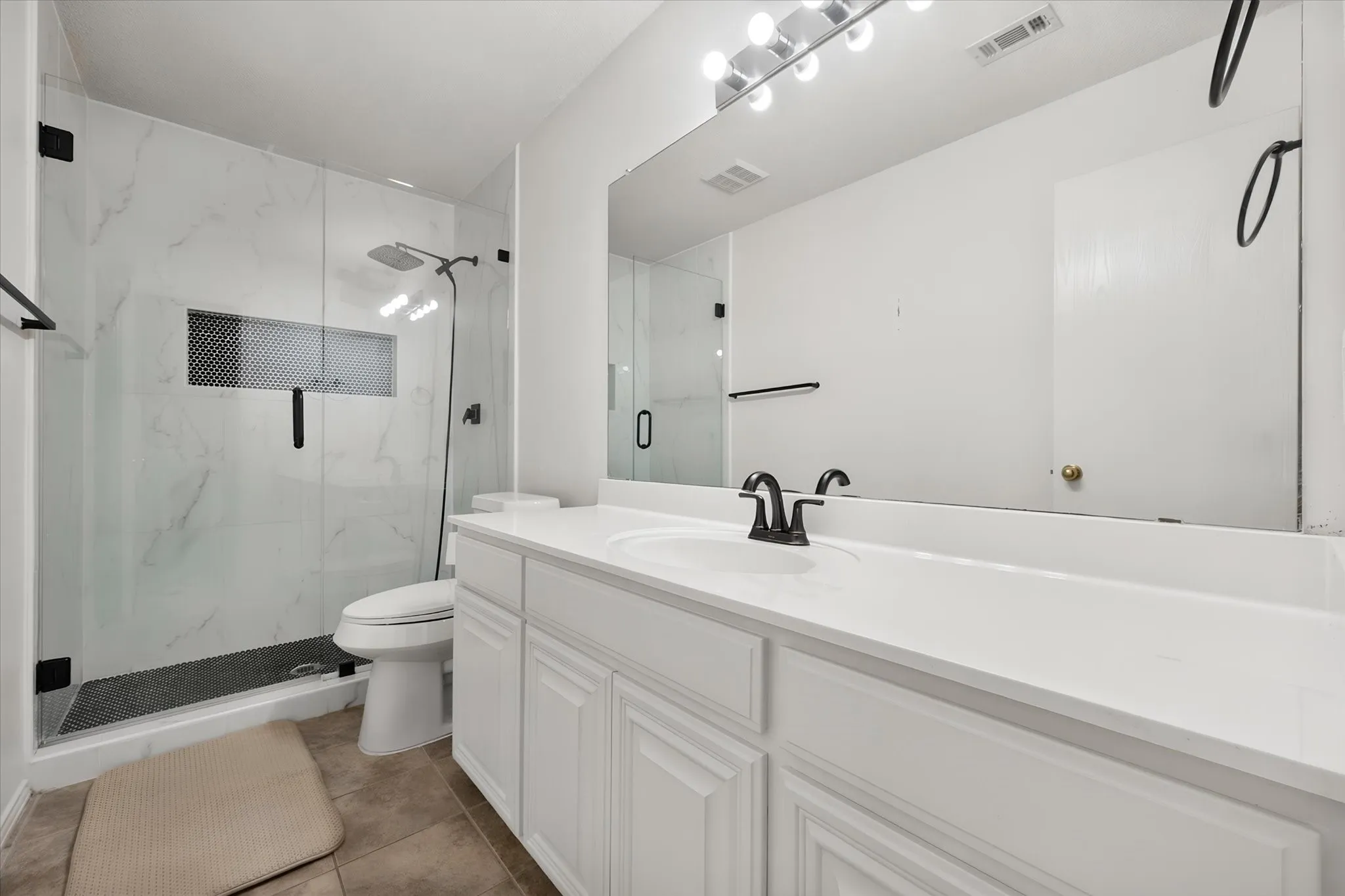 Walk-in shower with clear glass enclosure, white marble-patterned tile, and dark mosaic floor