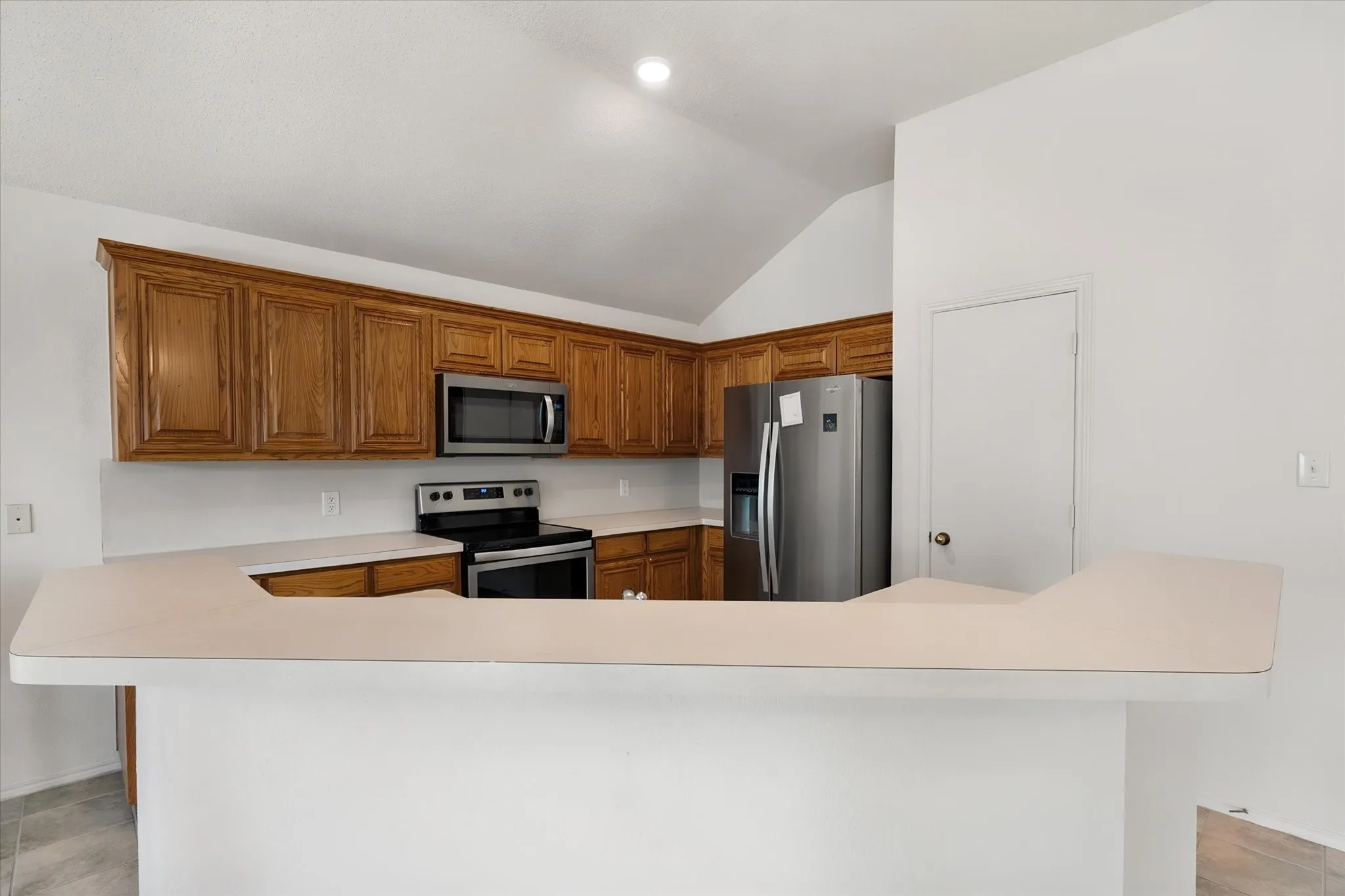 Kitchen featuring wood cabinetry, stainless steel appliances, white countertops, and a vaulted ceiling