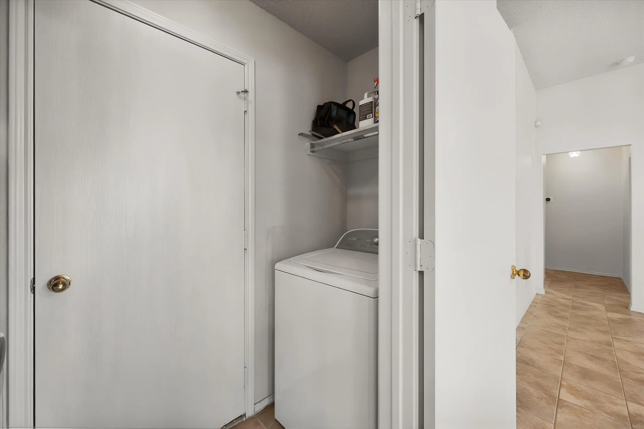 Laundry area with a top-load washing machine and an overhead storage shelf