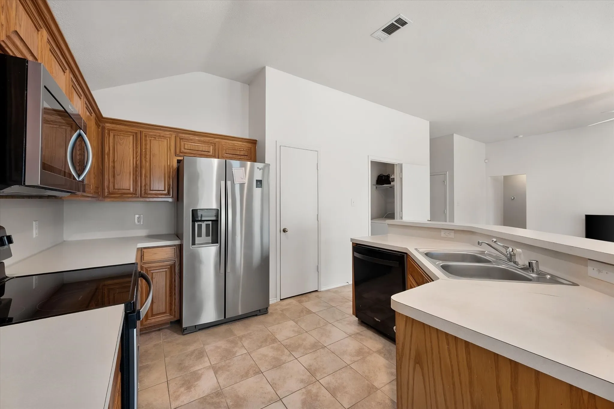 Kitchen featuring wood cabinetry, stainless steel refrigerator, black microwave, double basin sink, and tile flooring