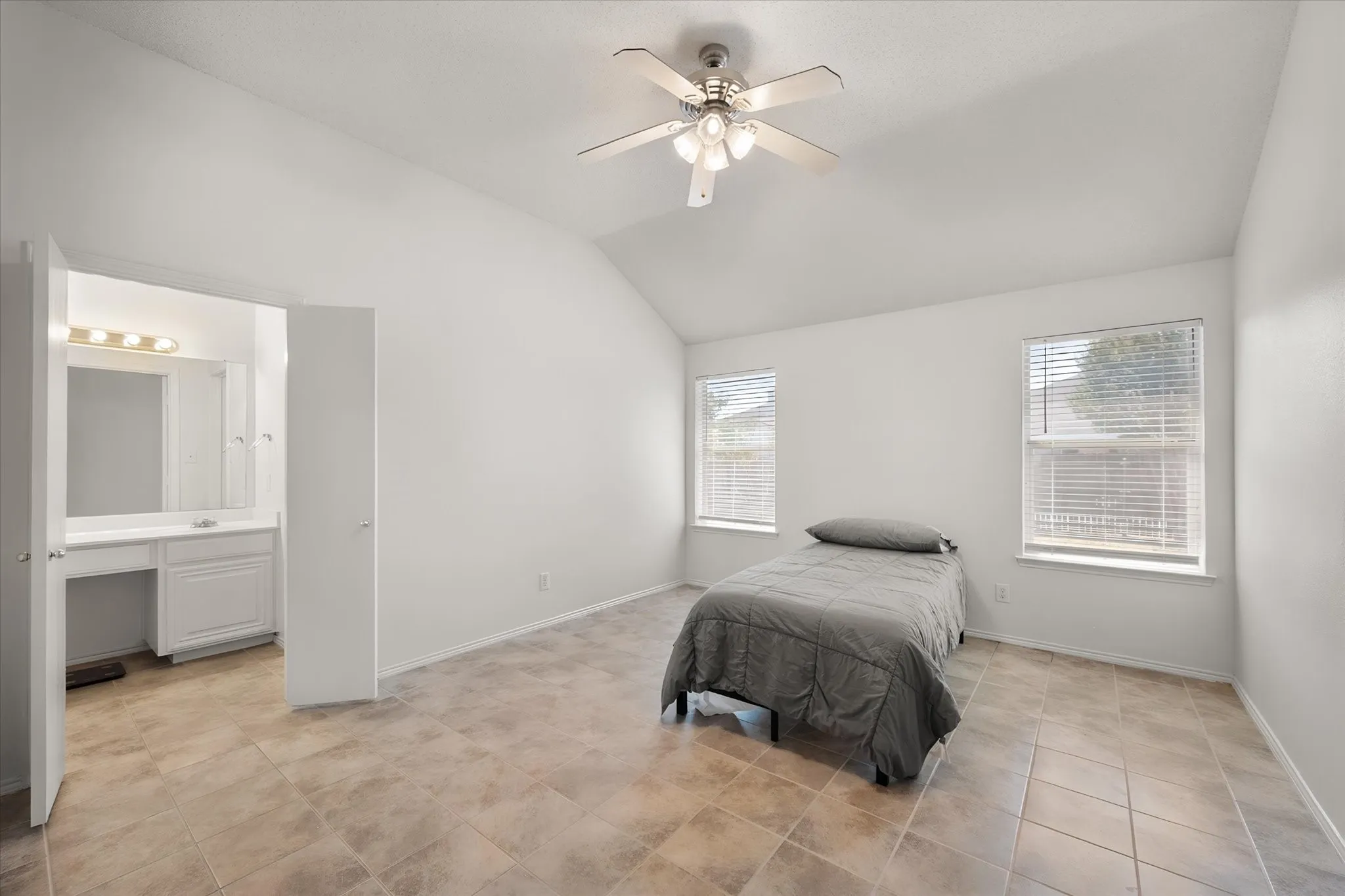 Vaulted ceiling with a ceiling fan, two windows with blinds, tiled flooring, and an attached vanity space with built-in cabinetry