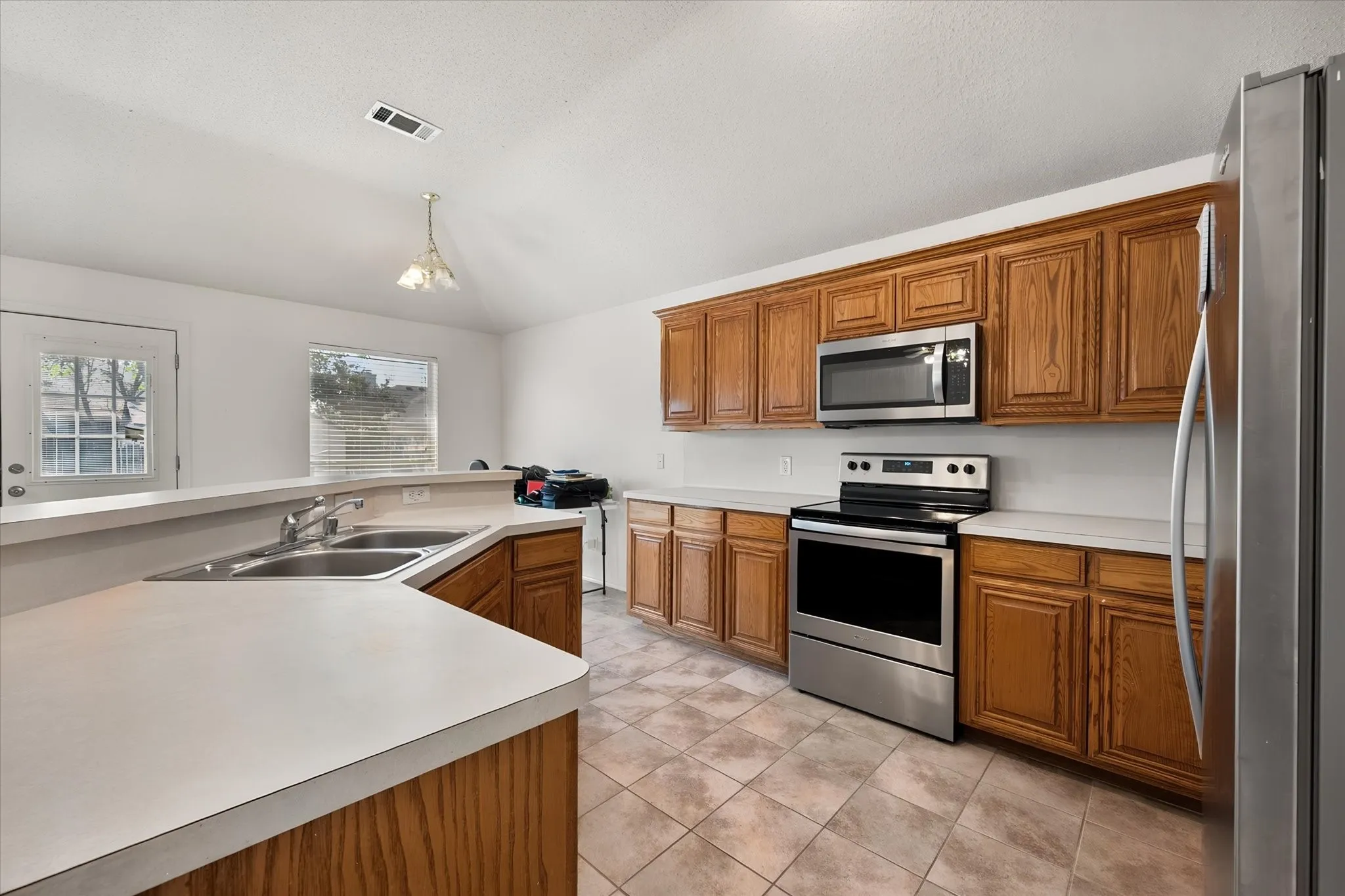 Kitchen featuring wood cabinetry, light-toned countertops, stainless steel appliances, and tiled flooring