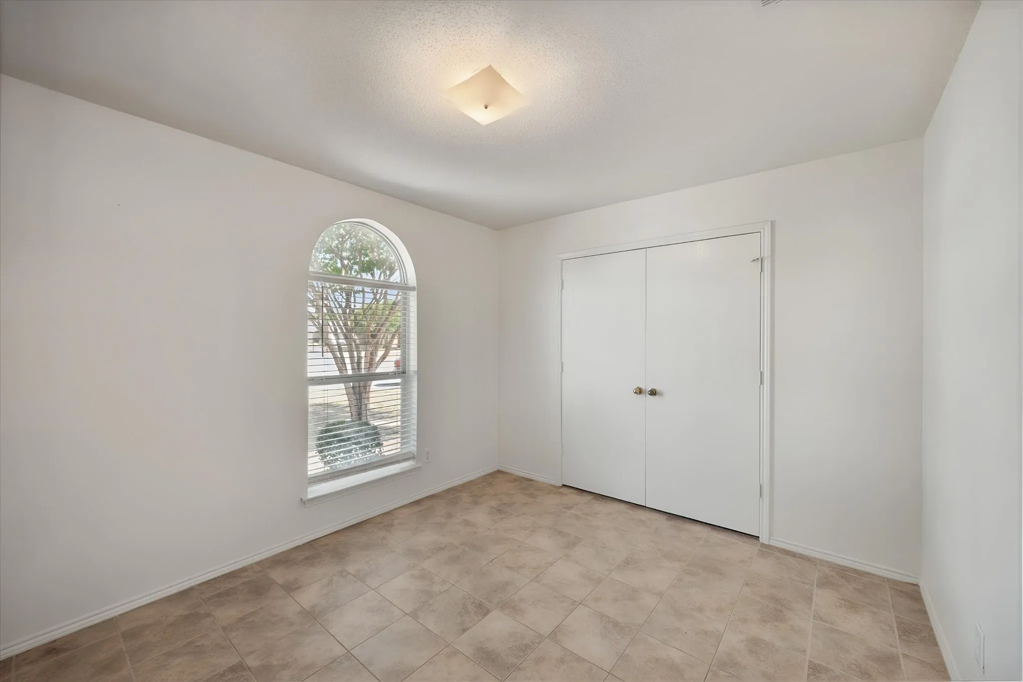 Arched window with blinds, bi-fold closet doors, square ceiling light fixture, and tile flooring