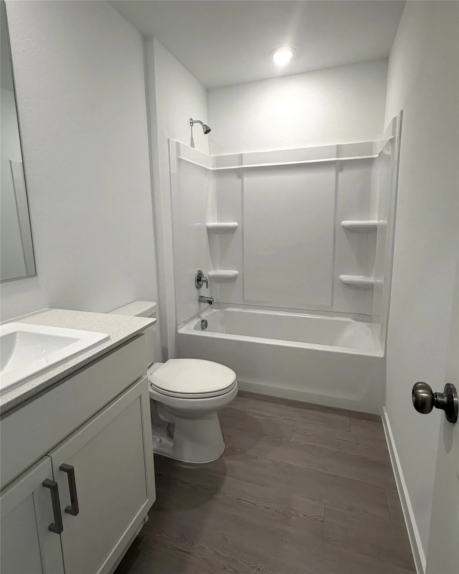 Bathroom featuring a white vanity with dark hardware, a white integrated sink, a light-colored countertop, a white toilet, a white tub with shower, and wood-finish flooring