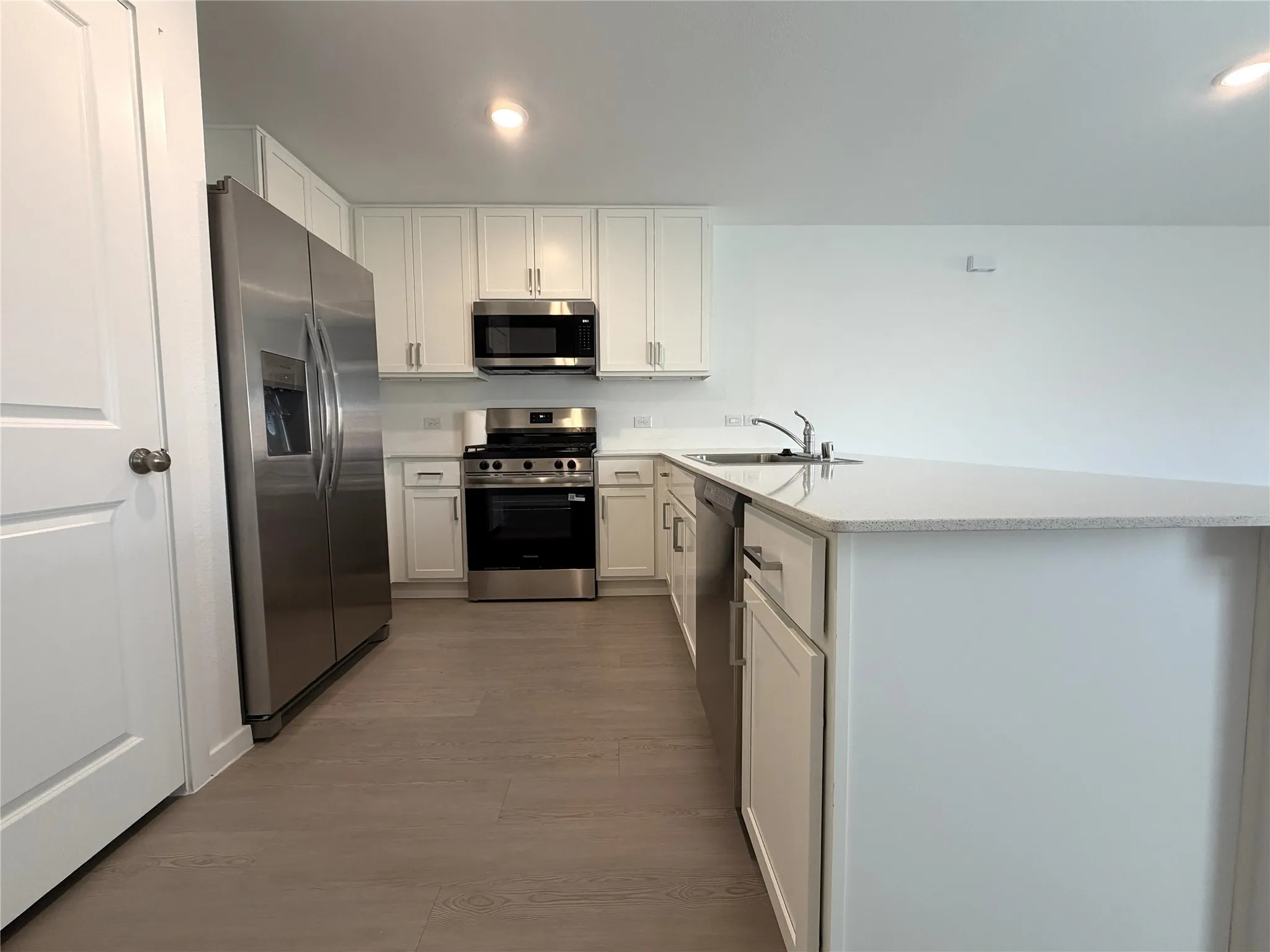 Kitchen featuring an island, white cabinetry, stainless steel appliances, wood-finish flooring, and light-toned countertops