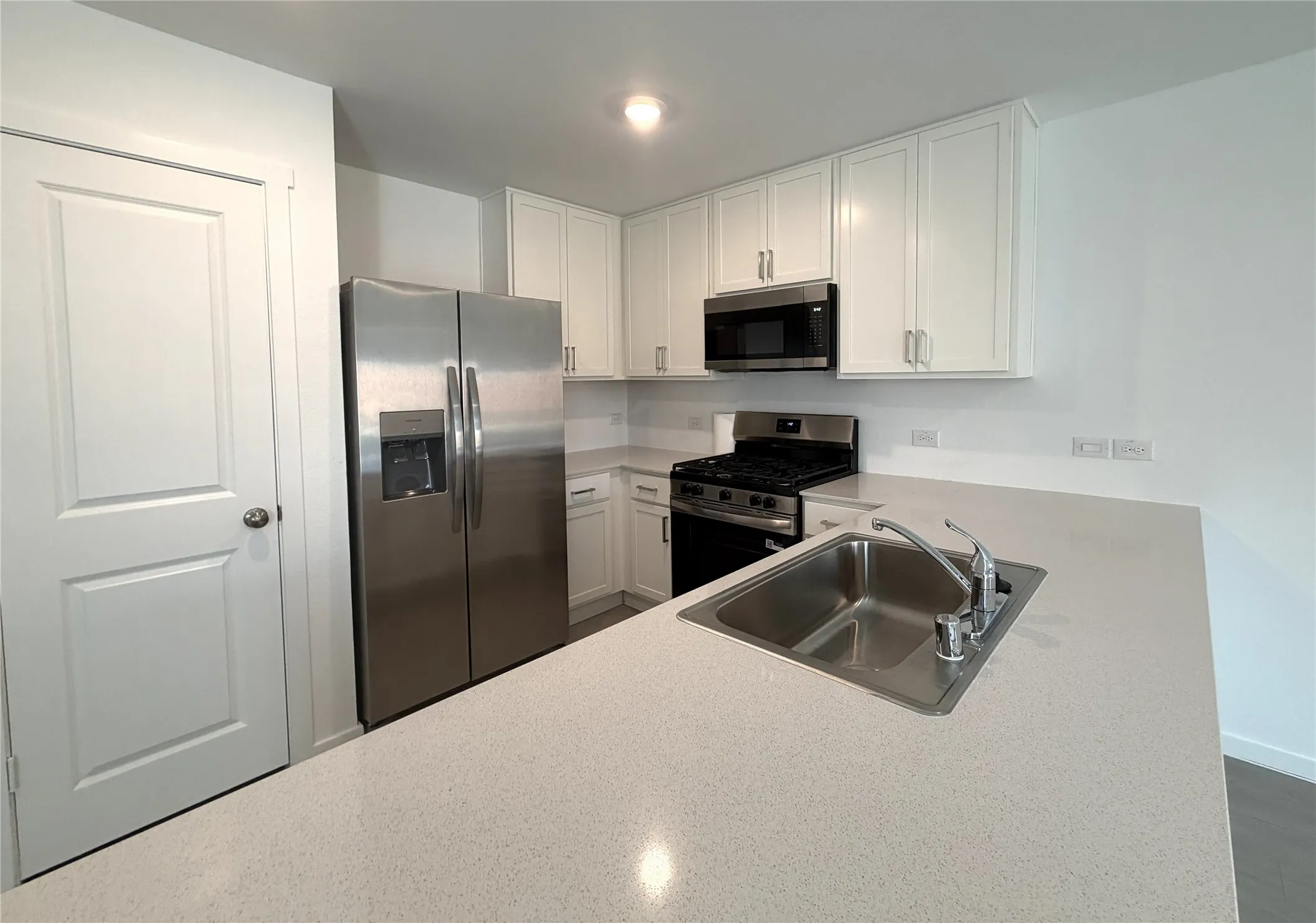 Contemporary kitchen featuring white cabinetry, stainless steel appliances, light-toned countertops, an undermount sink, and a built-in microwave