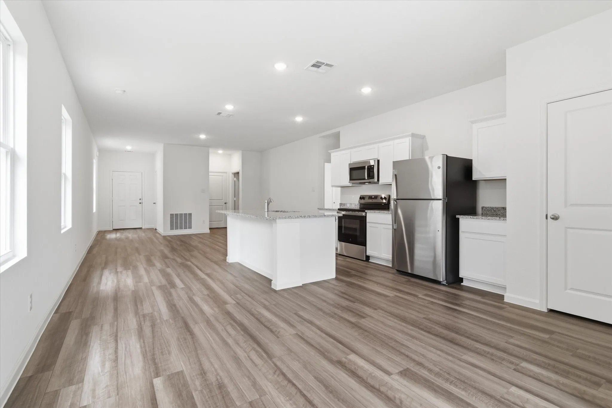 Open-concept living area featuring wood-finish flooring, recessed lighting, and multiple windows