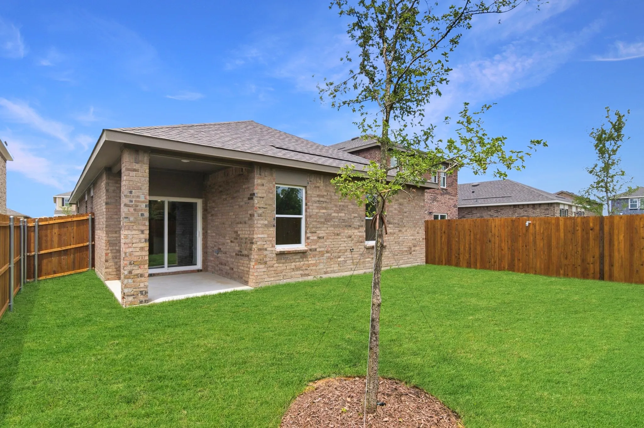 Brick exterior with covered patio, sliding glass door, and a private wood fence