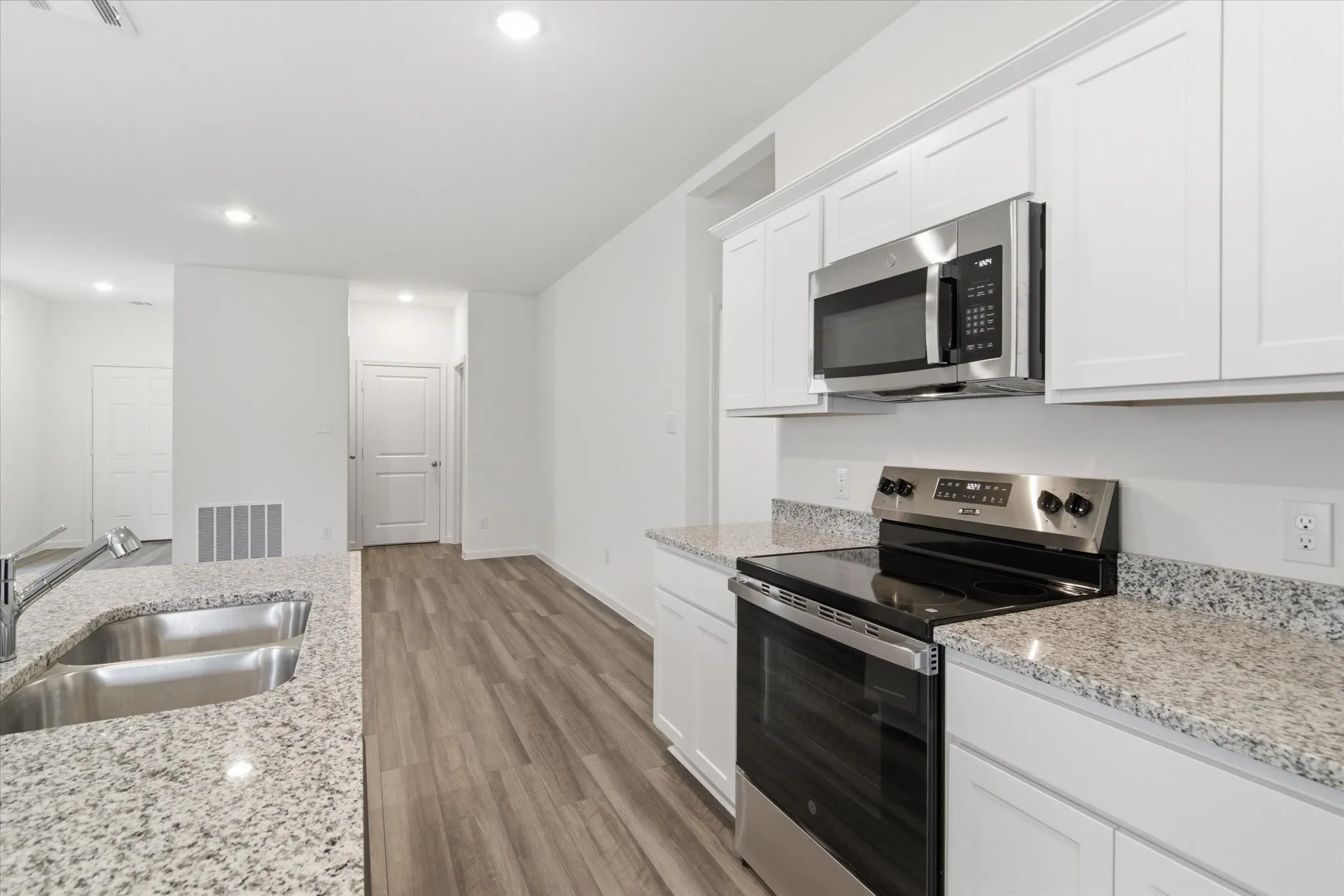 Kitchen featuring granite countertops, stainless steel appliances, white cabinetry, a double basin sink with a high arc faucet, and wood-finish flooring