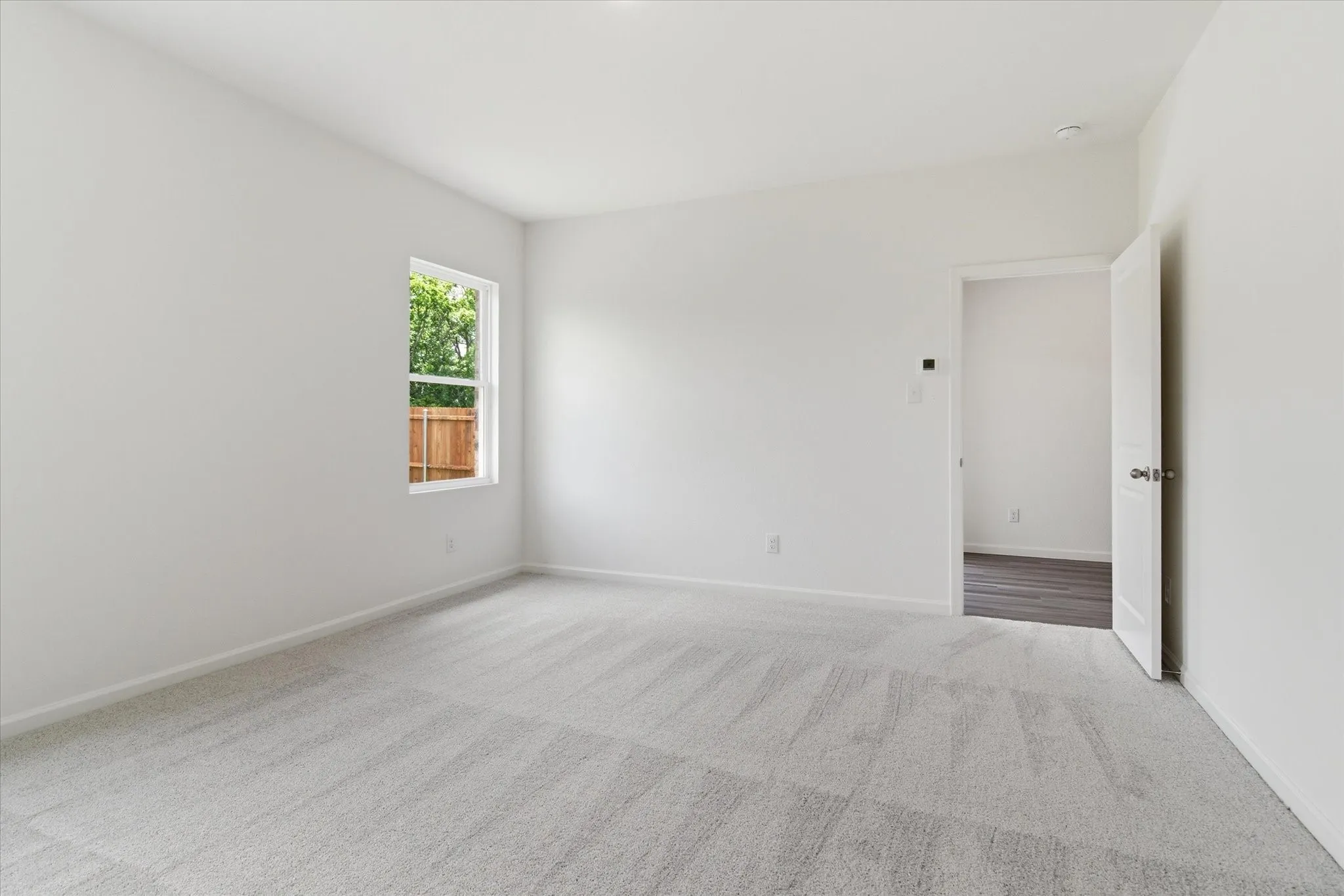 Neutral color palette, window with exterior view, light-toned carpet flooring, white walls, interior doorway