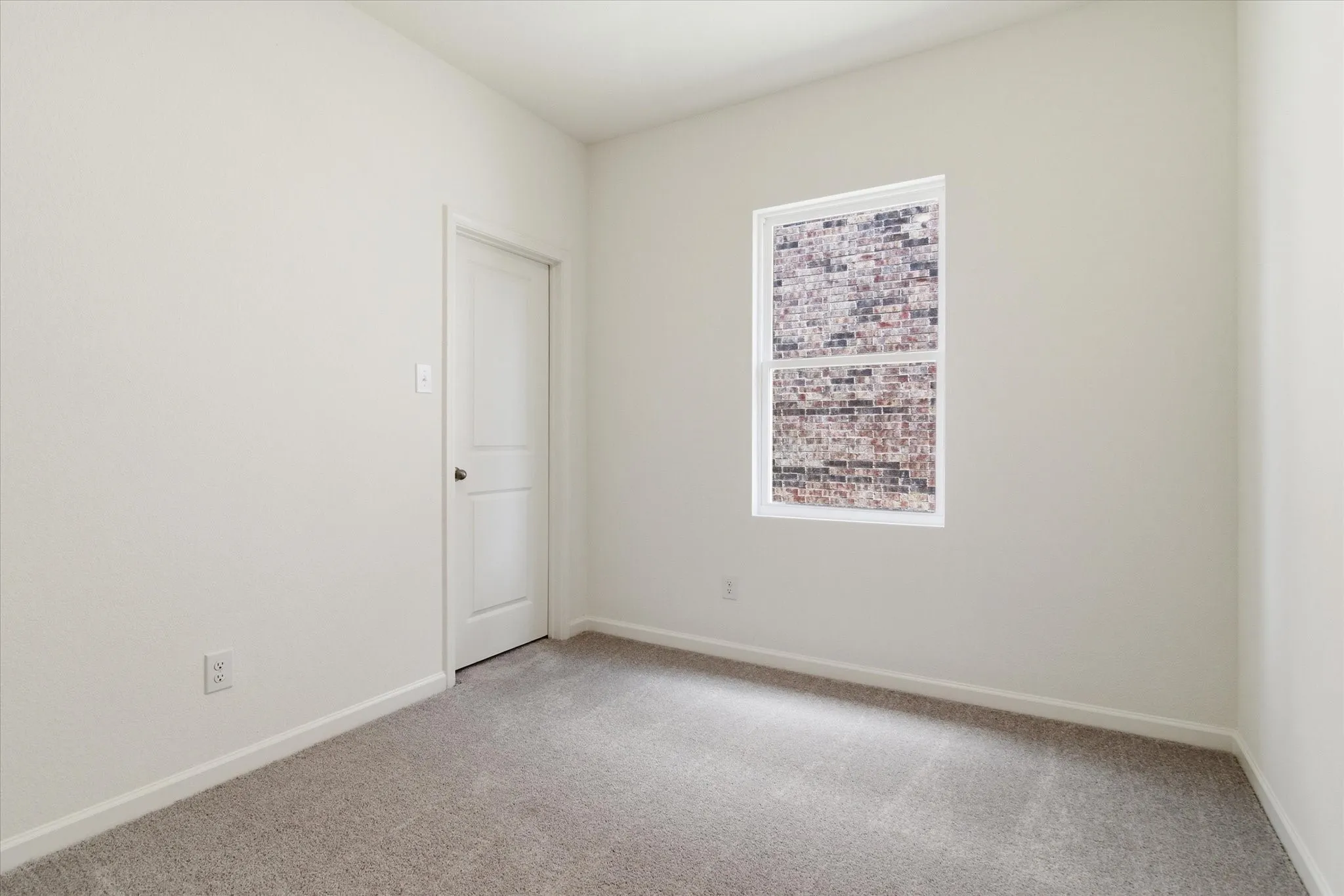 Neutral wall finishes with a single window and light grey carpeting
