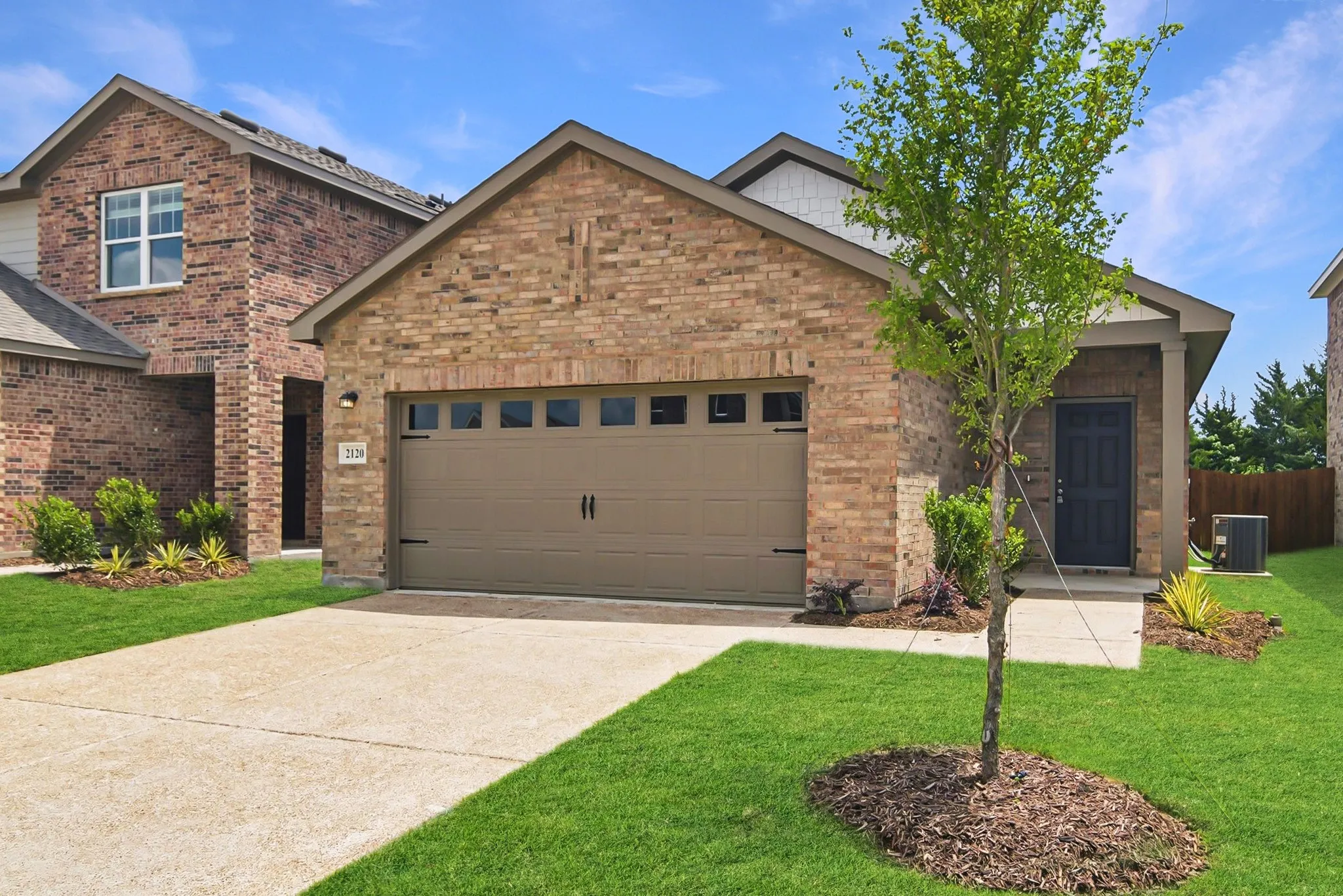 Brick exterior with contrasting siding accents, attached garage with window inserts, concrete driveway, front entrance, and established landscaping