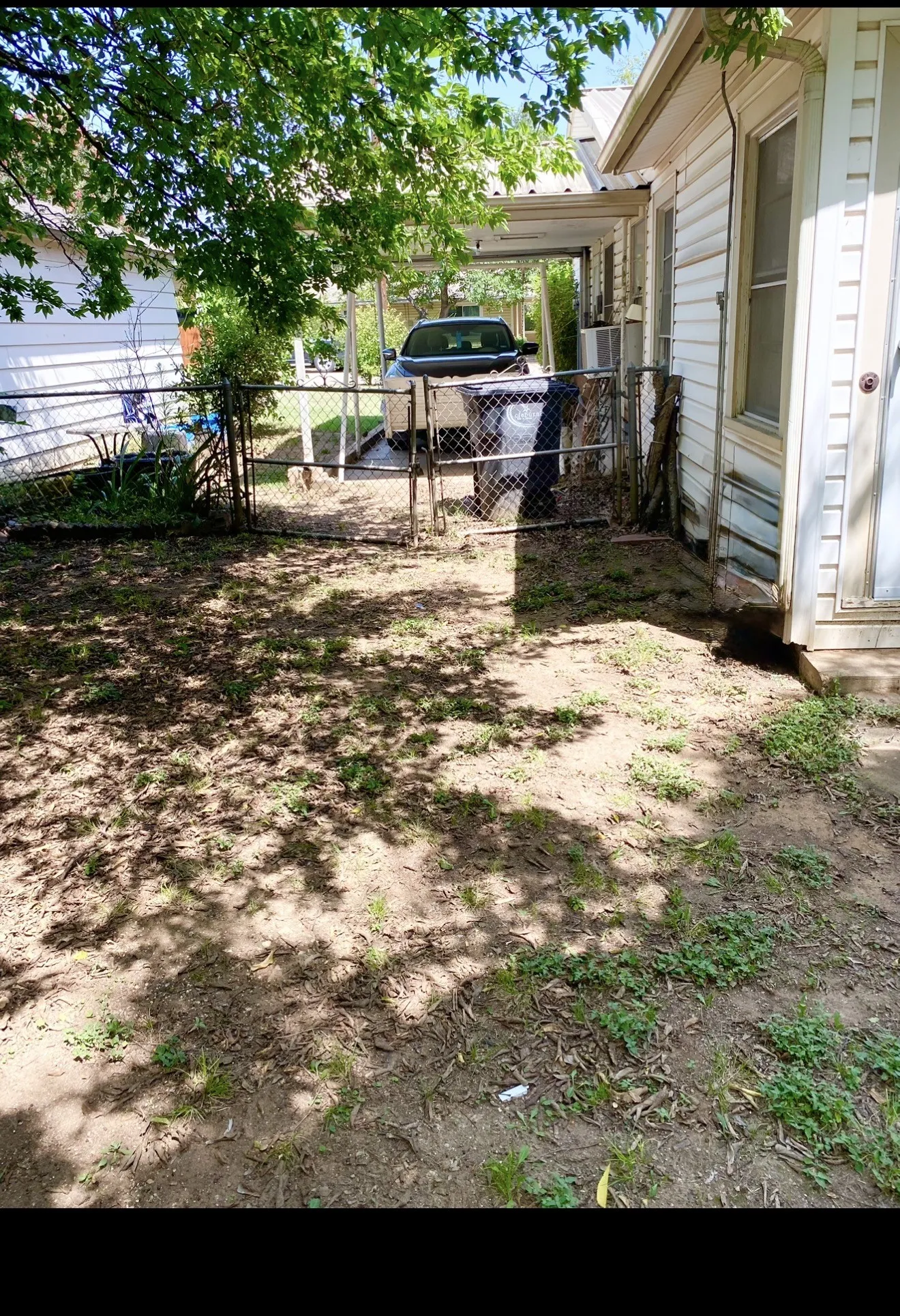 Chain link fencing with gate, carport structure, exterior siding, and an outdoor air conditioning unit