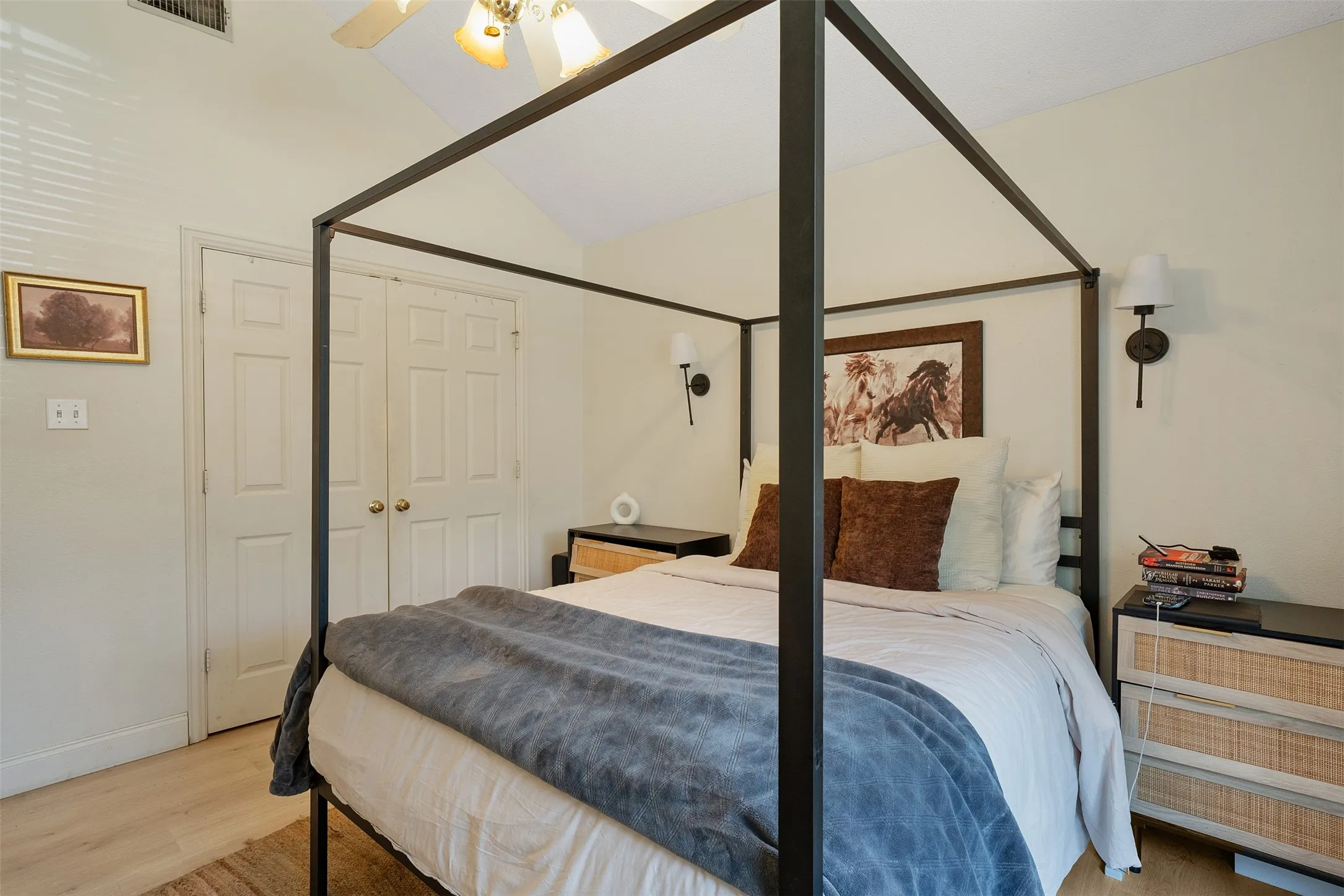 Vaulted ceiling with a ceiling fan, dual bi-fold doors, wood-finish flooring, and wall-mounted sconces