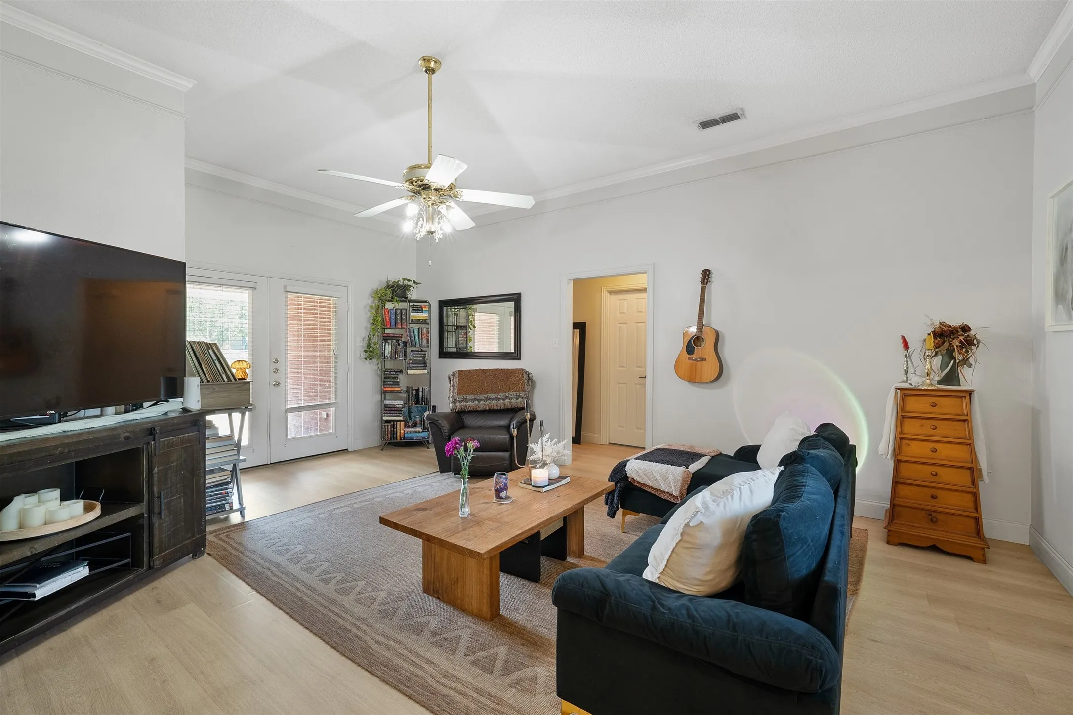 Spacious living area featuring wood-finish flooring, a ceiling fan, and crown molding