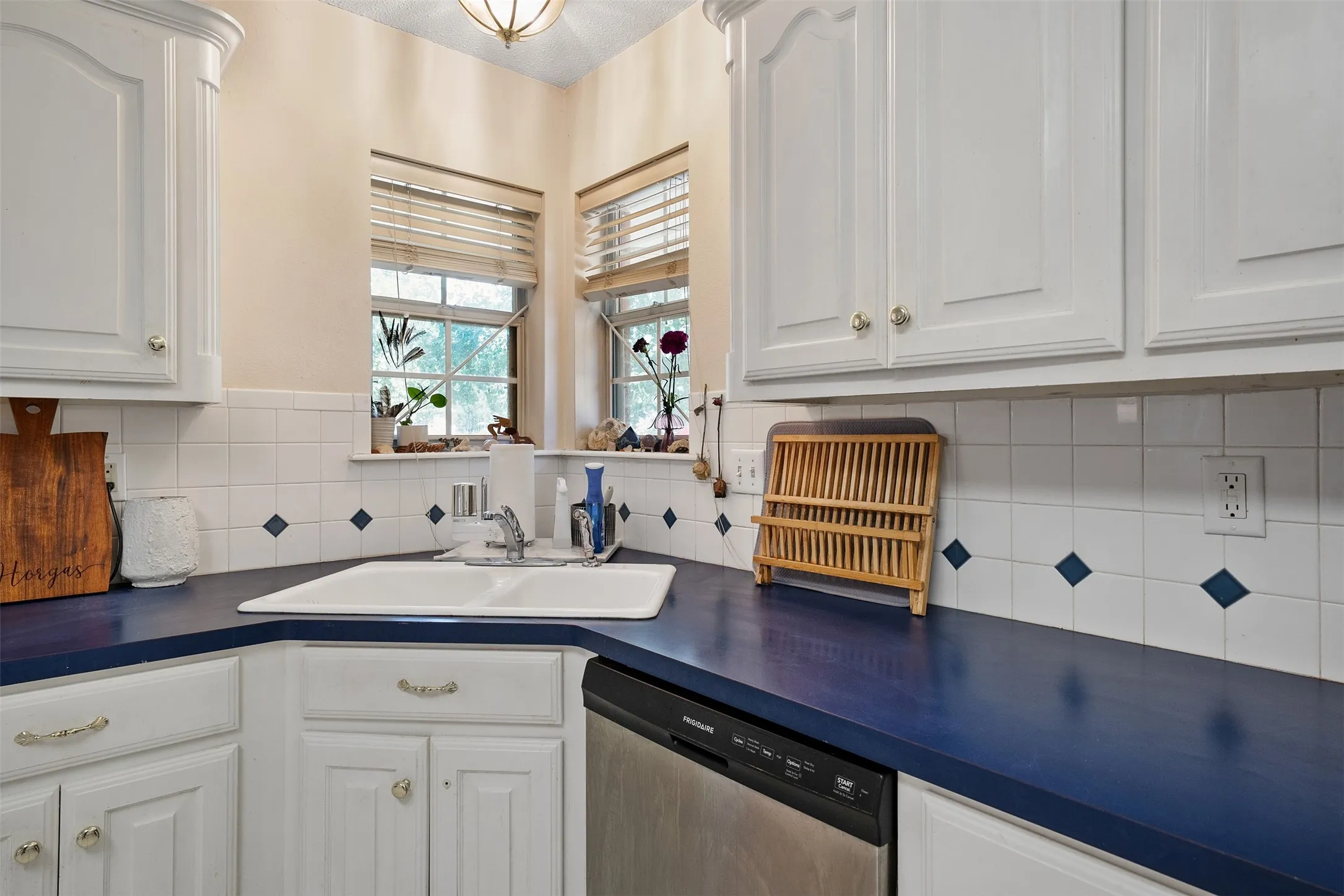 White cabinetry with decorative hardware, a double basin sink, blue countertops, and a white tile backsplash with blue accents
