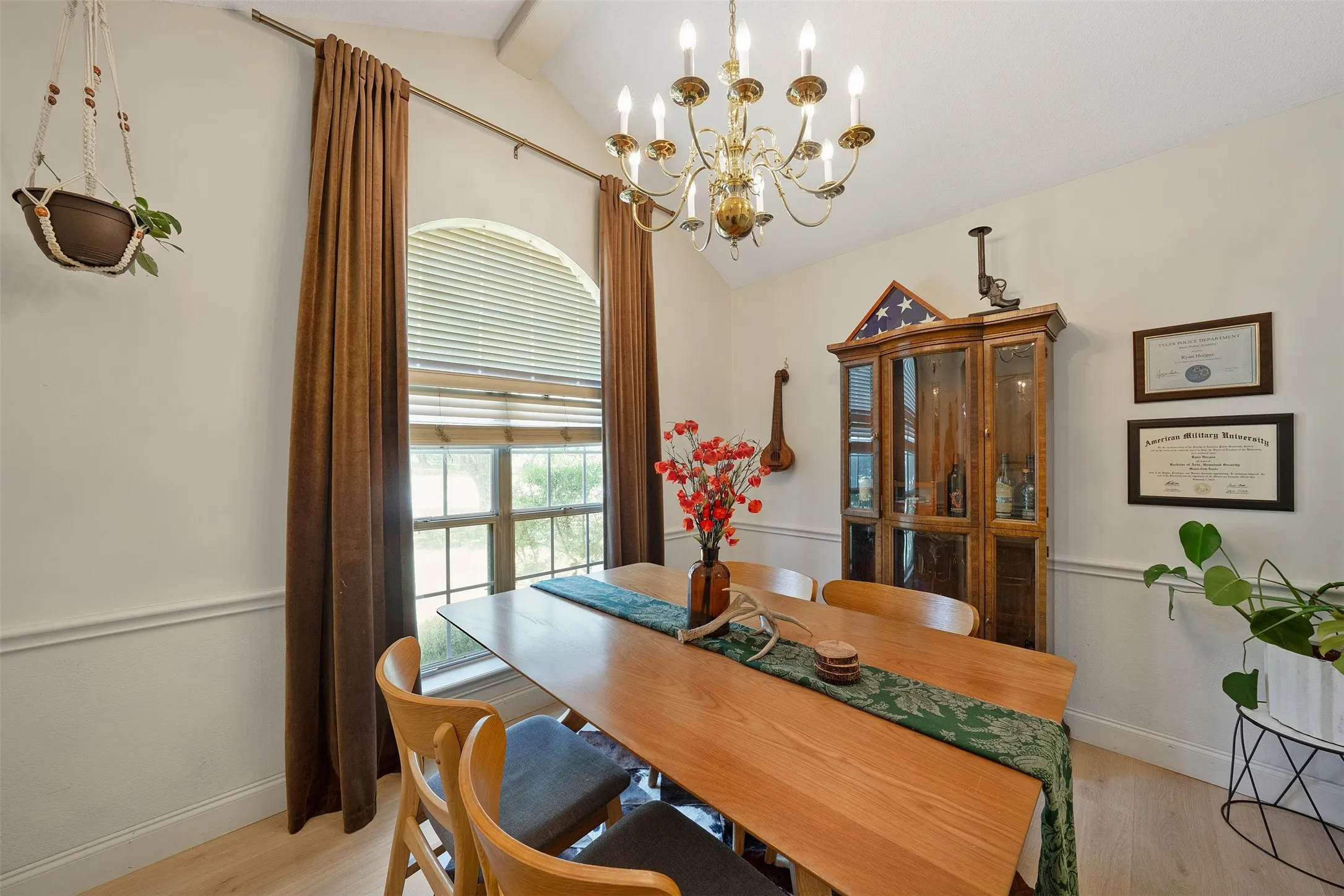 Vaulted ceiling, arched window with blinds, decorative chair rail molding, wood-finish flooring, and a brass chandelier