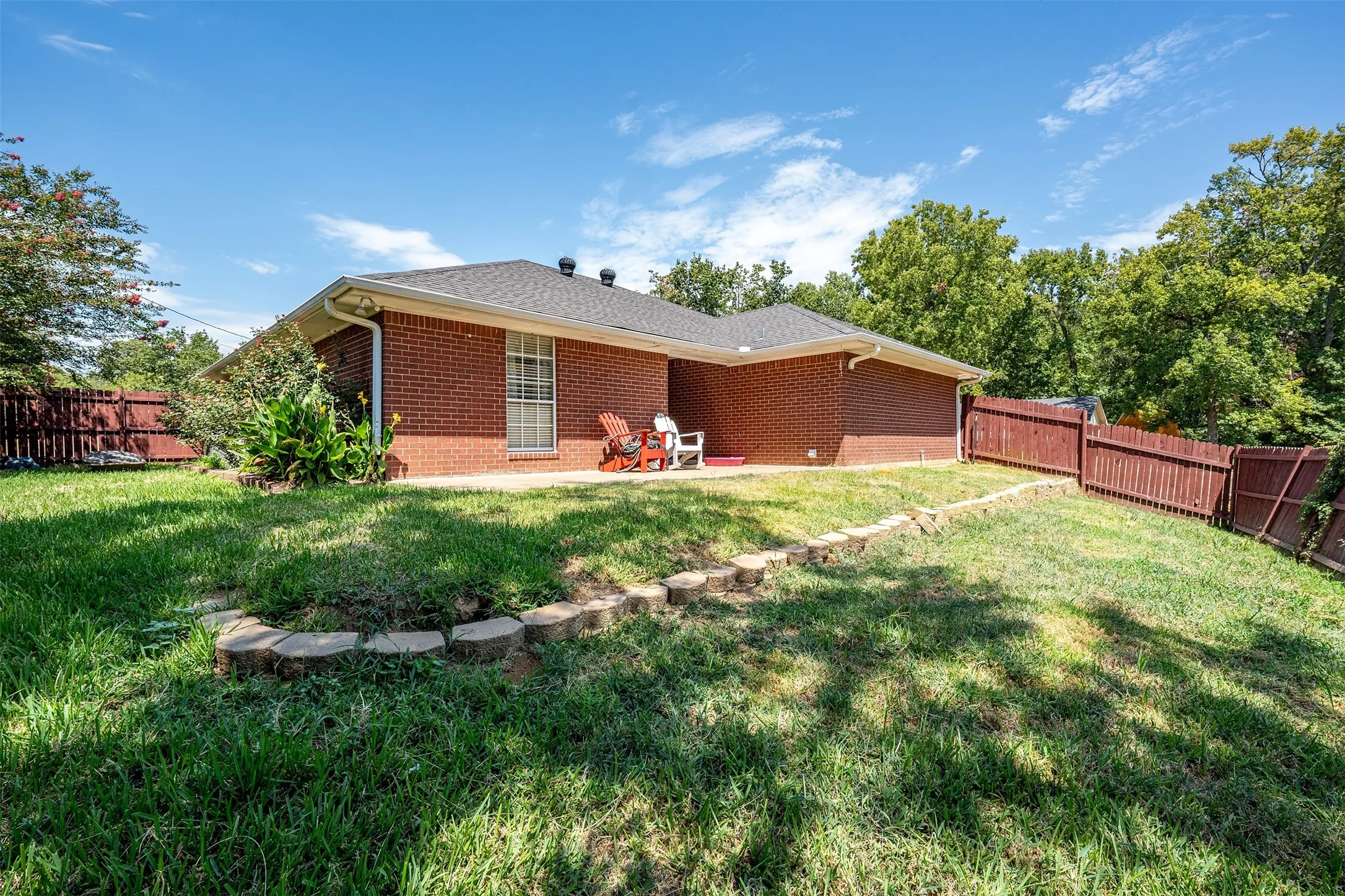 Brick exterior, dark shingle roof, white trim, privacy fencing, and a concrete patio