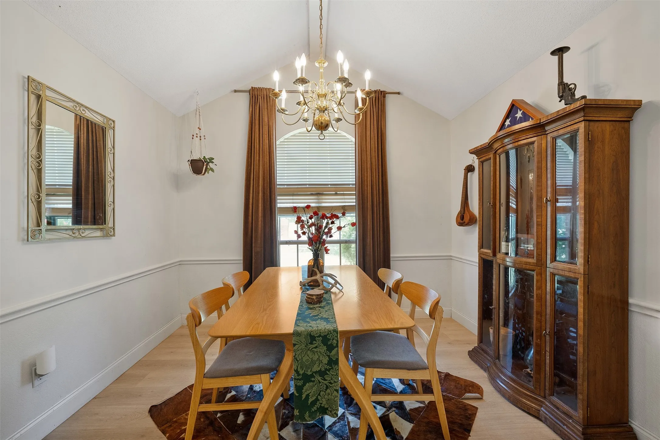 Vaulted ceiling with an ornate chandelier, arched window with blinds, chair rail molding, and wood-finish flooring