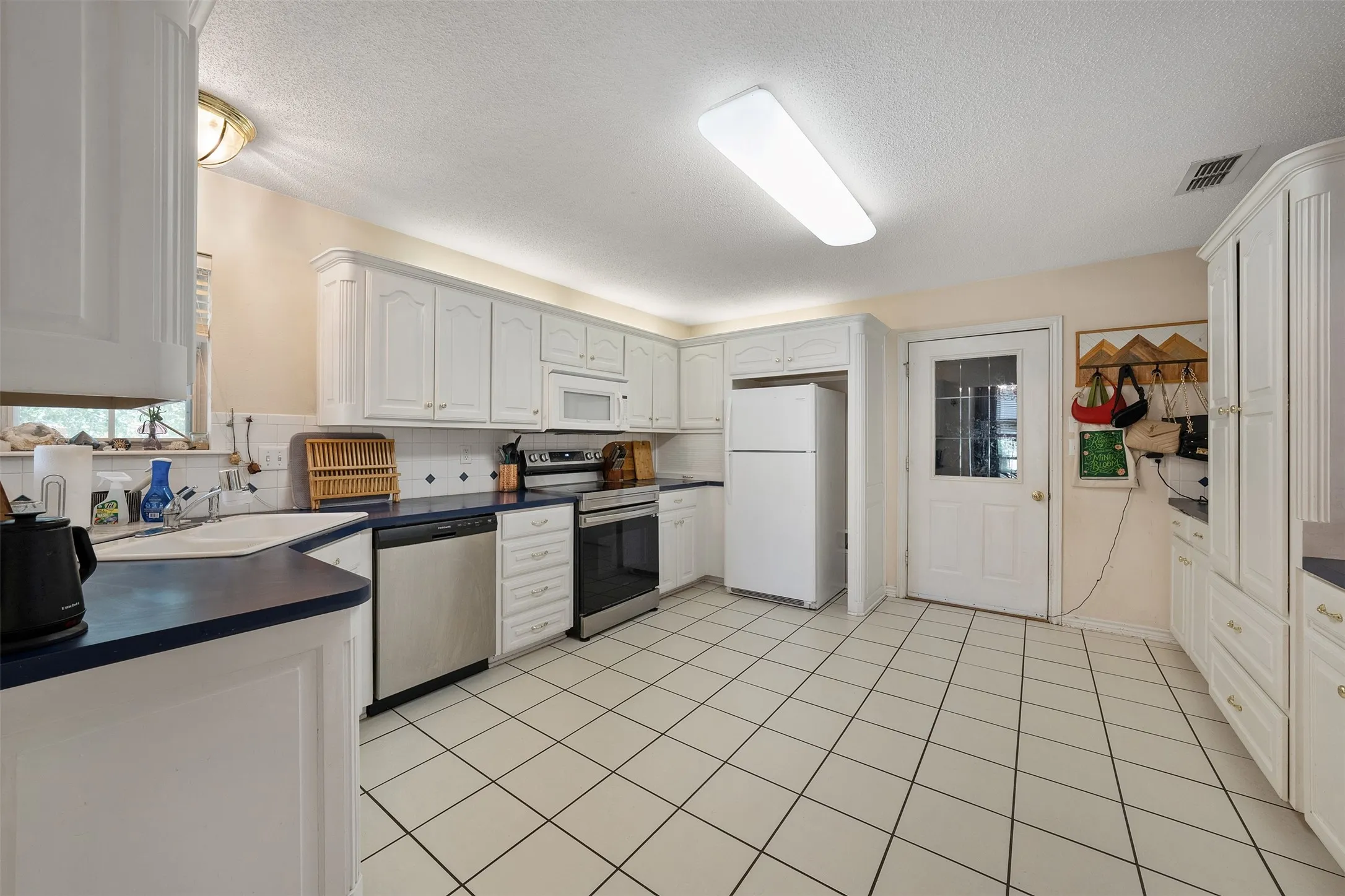 White cabinetry, stainless steel appliances, ceramic tile flooring, and a glass-paneled exterior door