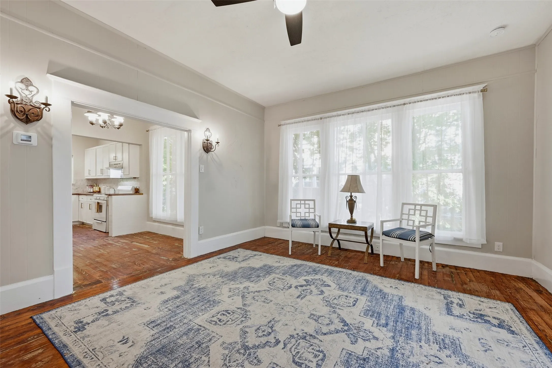 Expansive wood-finish flooring, three large windows, recessed lighting, and decorative wall sconces
