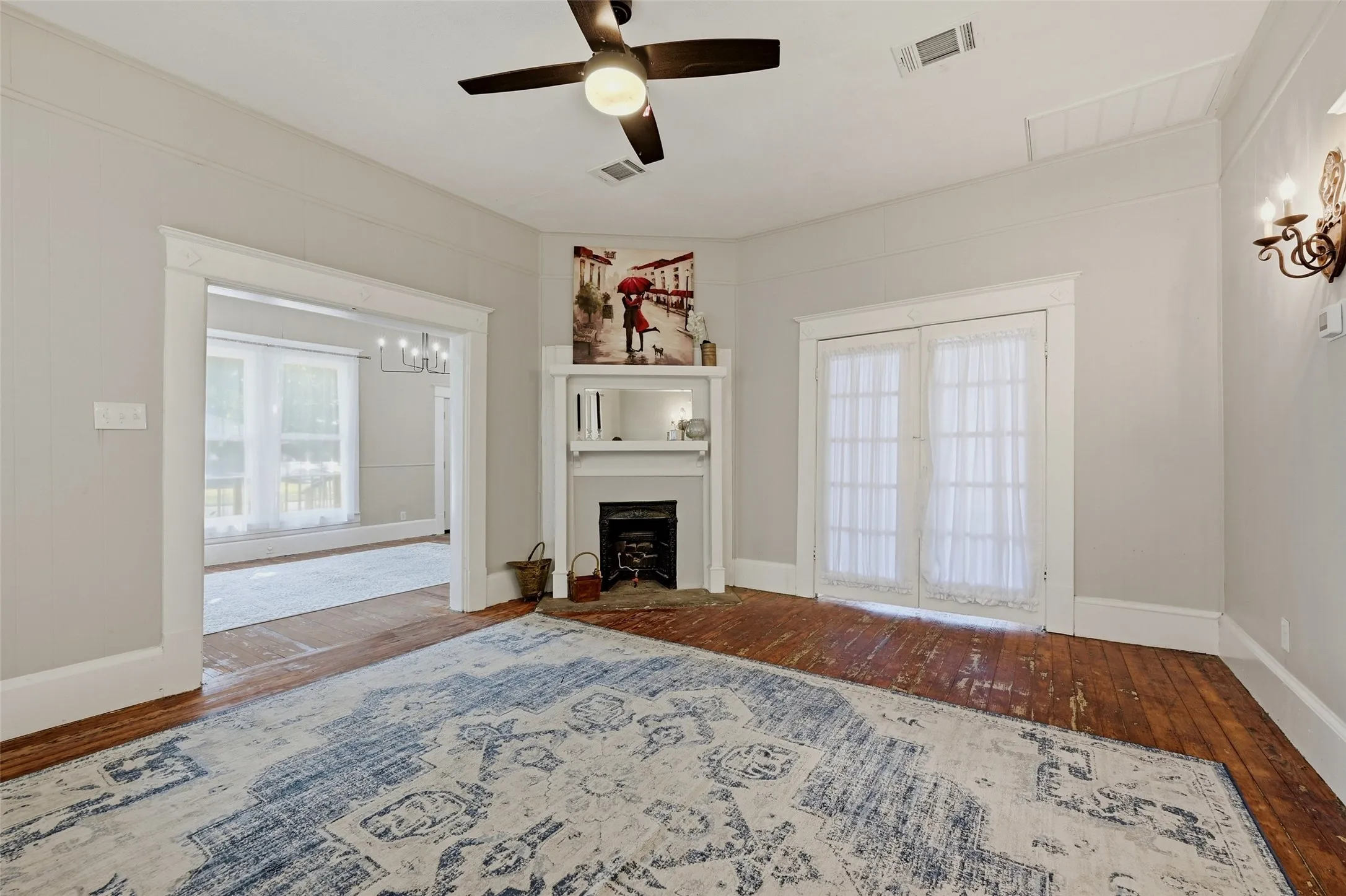 Hardwood flooring, painted interior walls, fireplace with mantel, ceiling fan, and sconce lighting