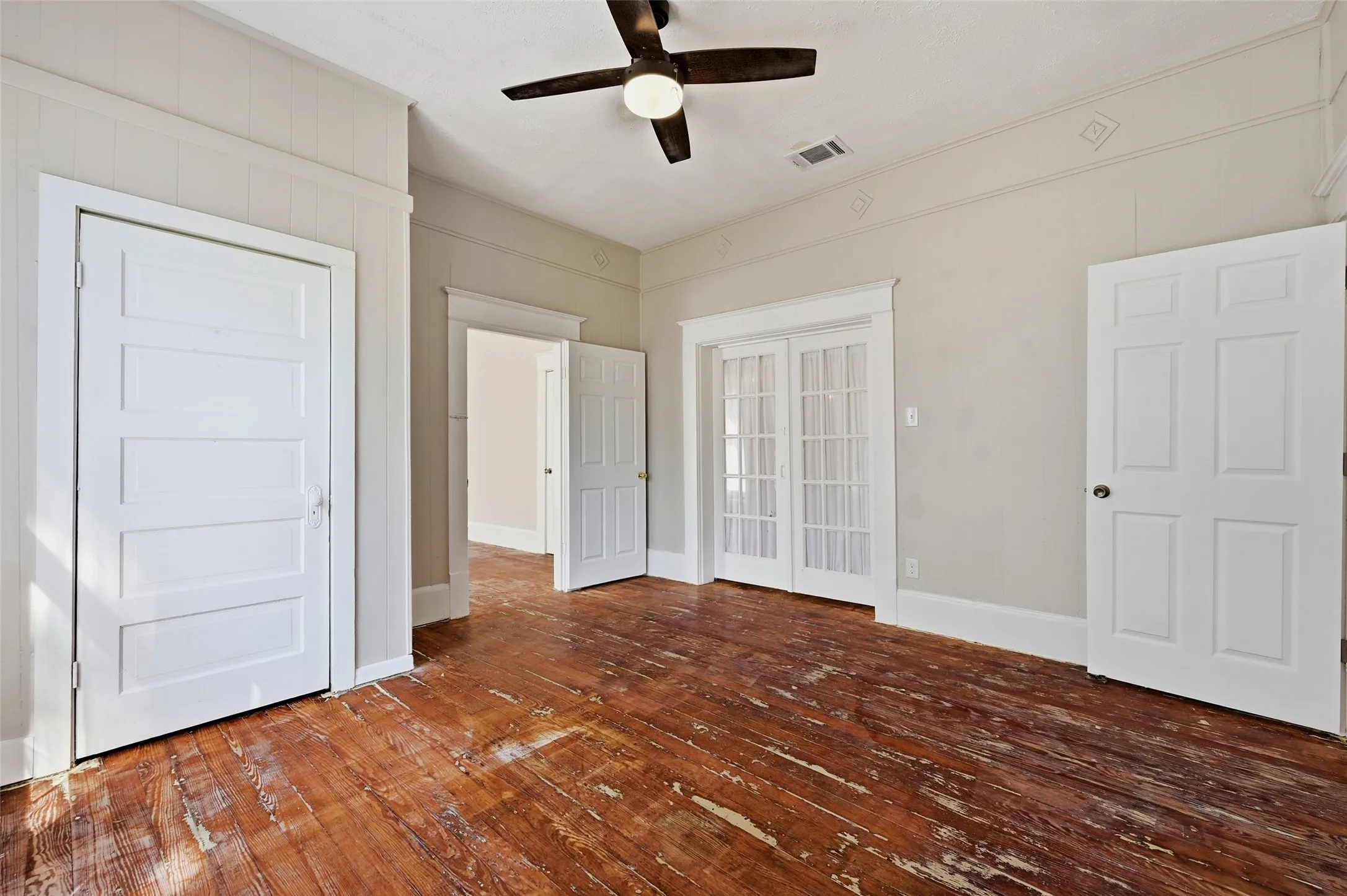 Wood-finish flooring, ceiling fan, white paneled doors, and French doors