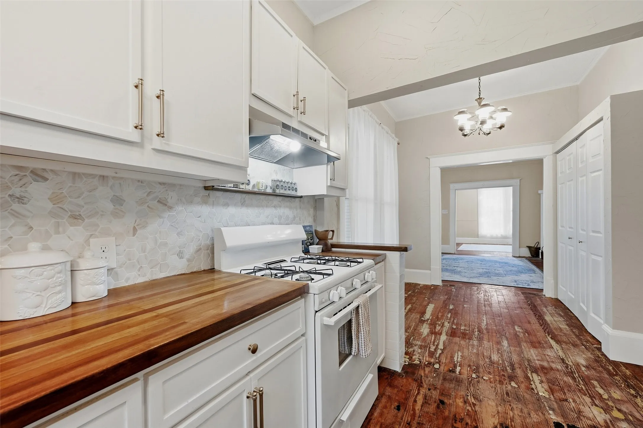 White cabinetry, wood countertops, stone mosaic tile backsplash, gas range, and warm wood flooring