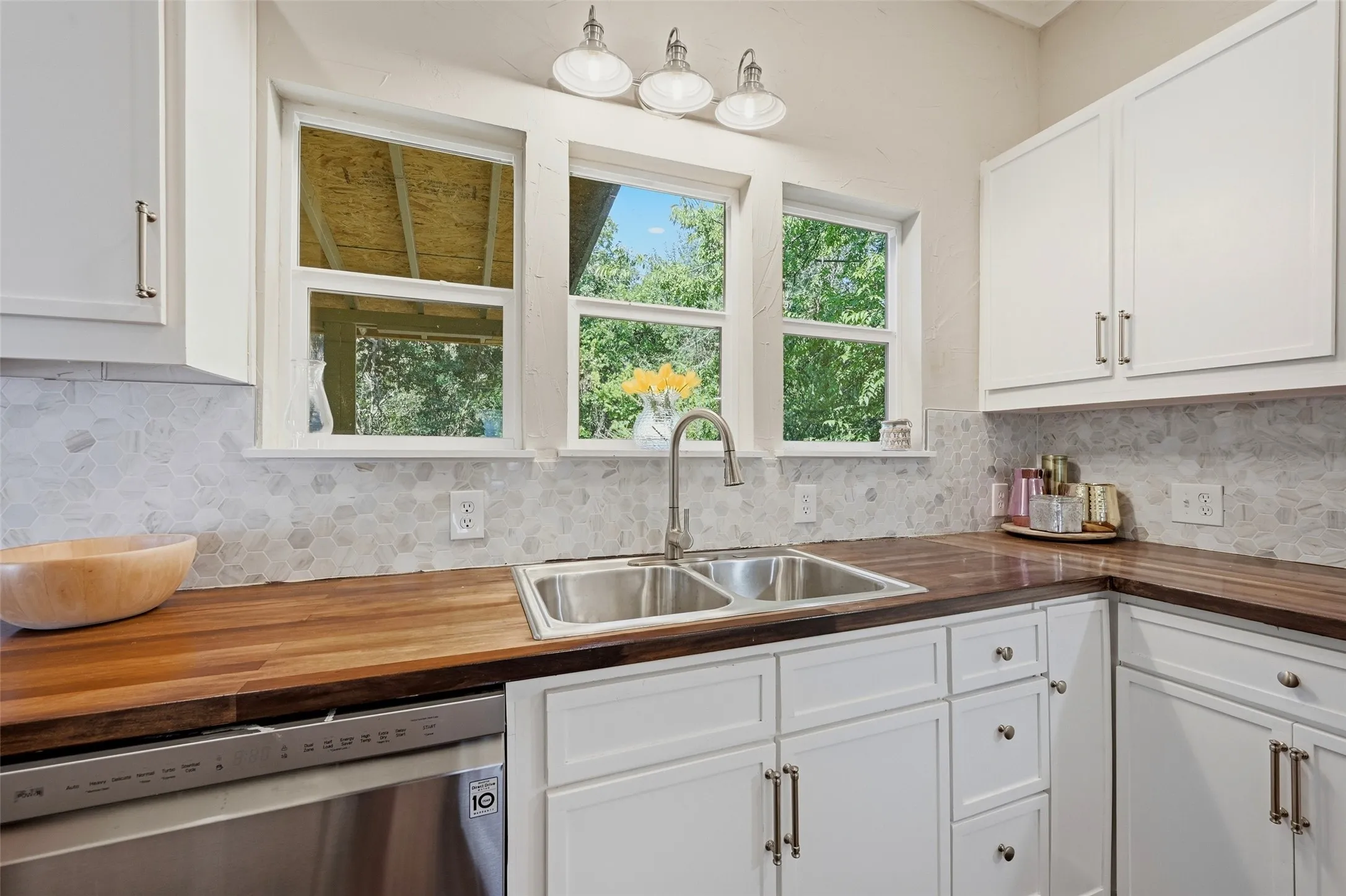 White cabinetry with brushed nickel hardware, natural wood countertops, stainless steel double basin sink with a gooseneck faucet, and a hexagonal tile backsplash
