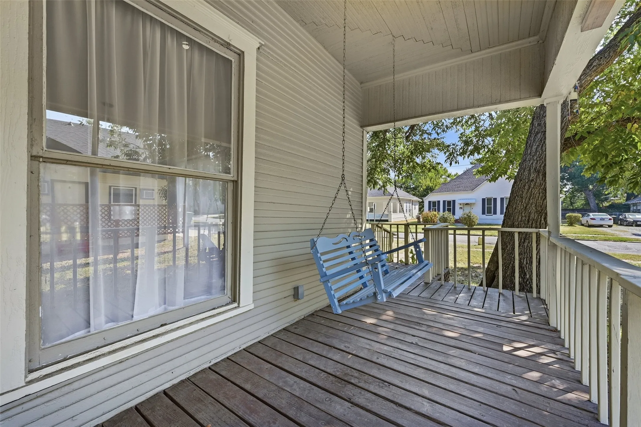 Covered front porch with wood-finish flooring, white railing, and exterior siding