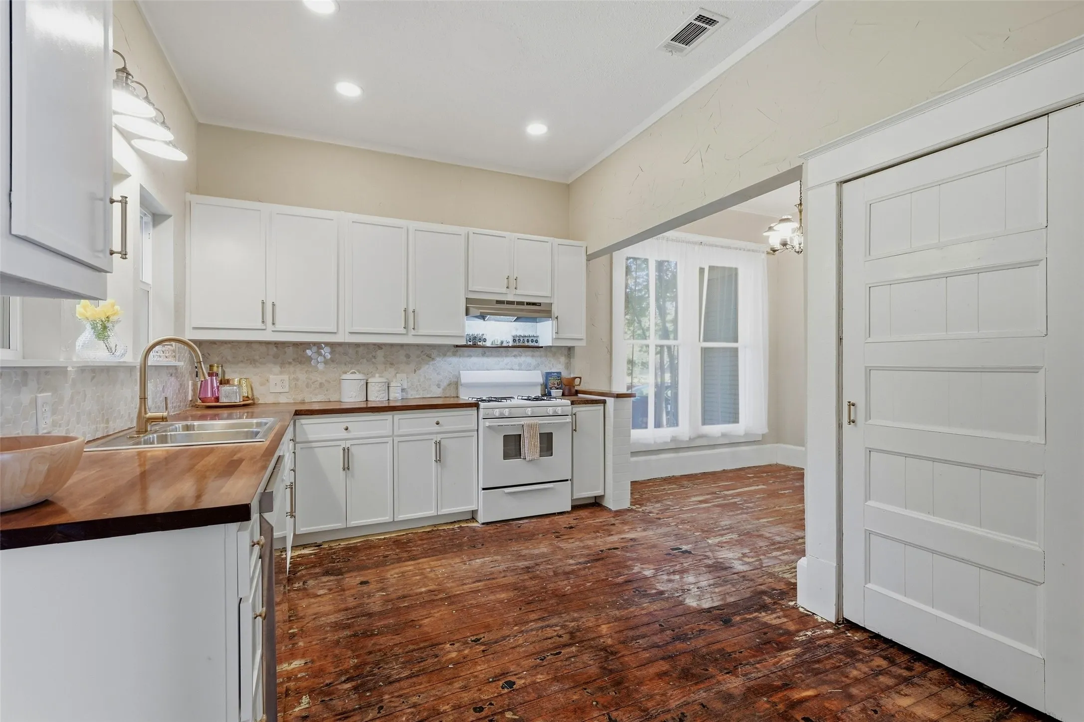 White cabinetry with gold-finish hardware, built-in stainless steel sink, wood countertops, and tile backsplash